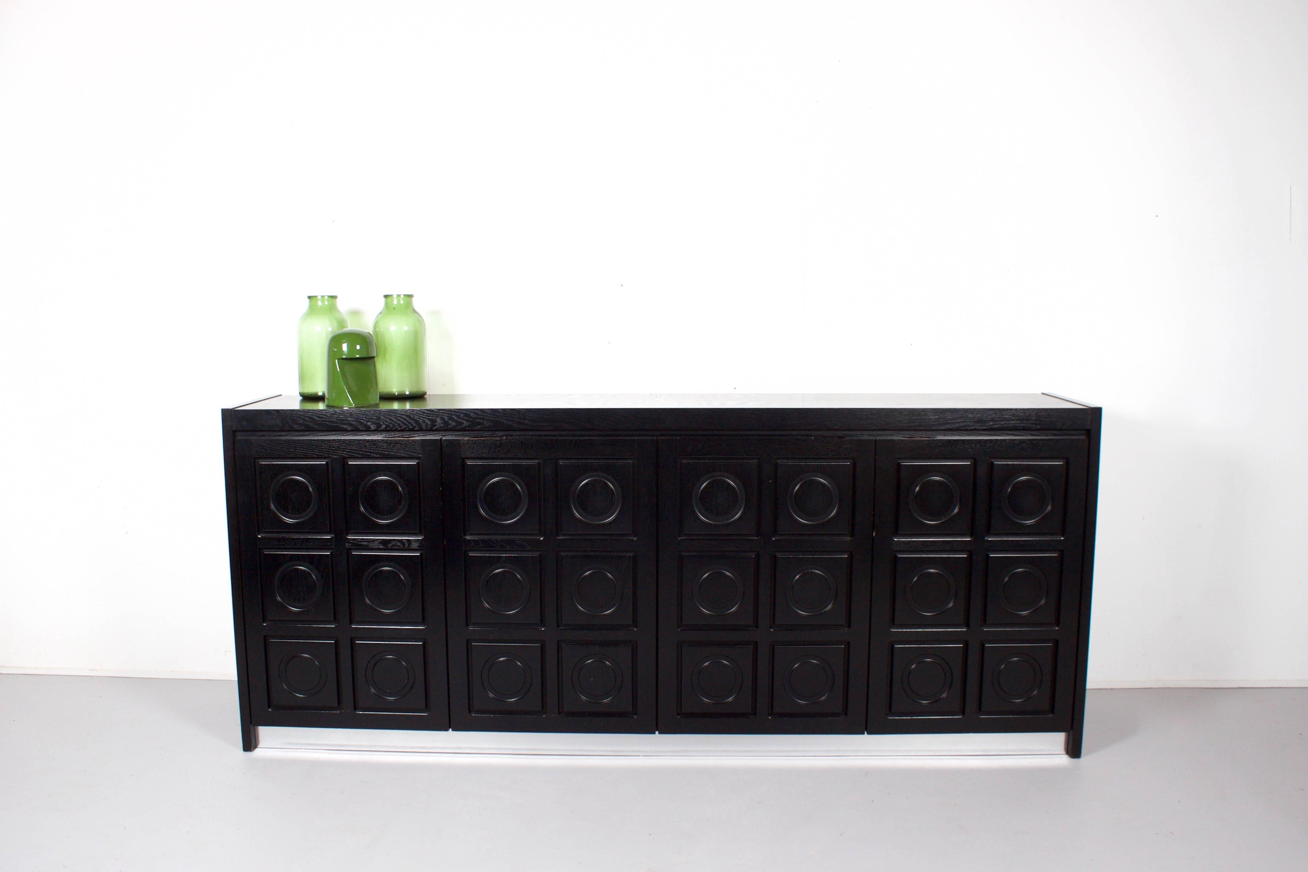 Impressive Belgium Brutalist credenza in very good condition

This sideboard has four doors made of massive black stained oak, each with a three-dimensional pattern of circles.

The sideboard is equipped with an aluminium strip on the base which