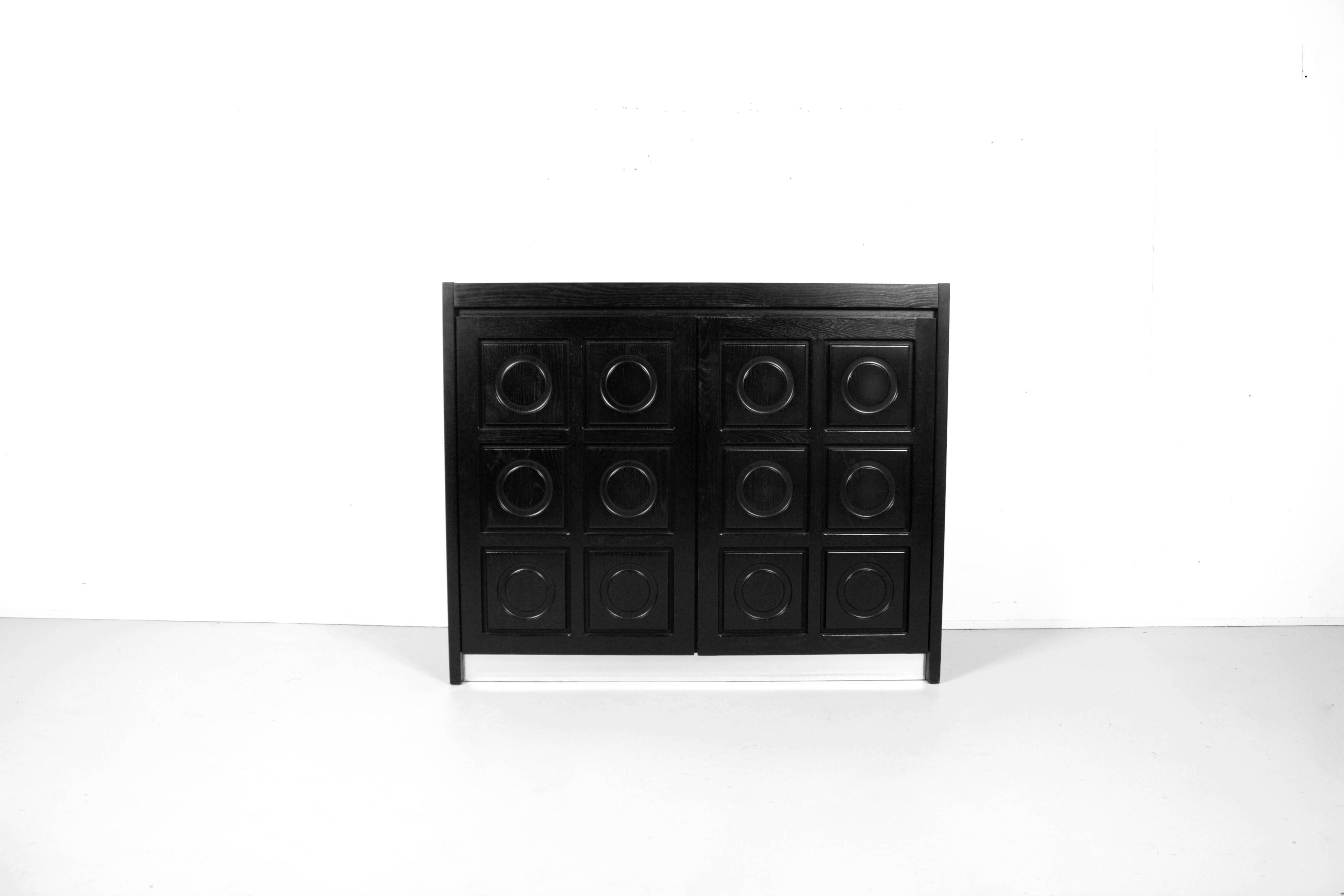 Belgium Brutalist credenza in very good condition

This sideboard has two doors made of massive black stained oak, each with a three-dimensional pattern of circles.

The sideboard is equipped with a aluminium strip on the base which gives a