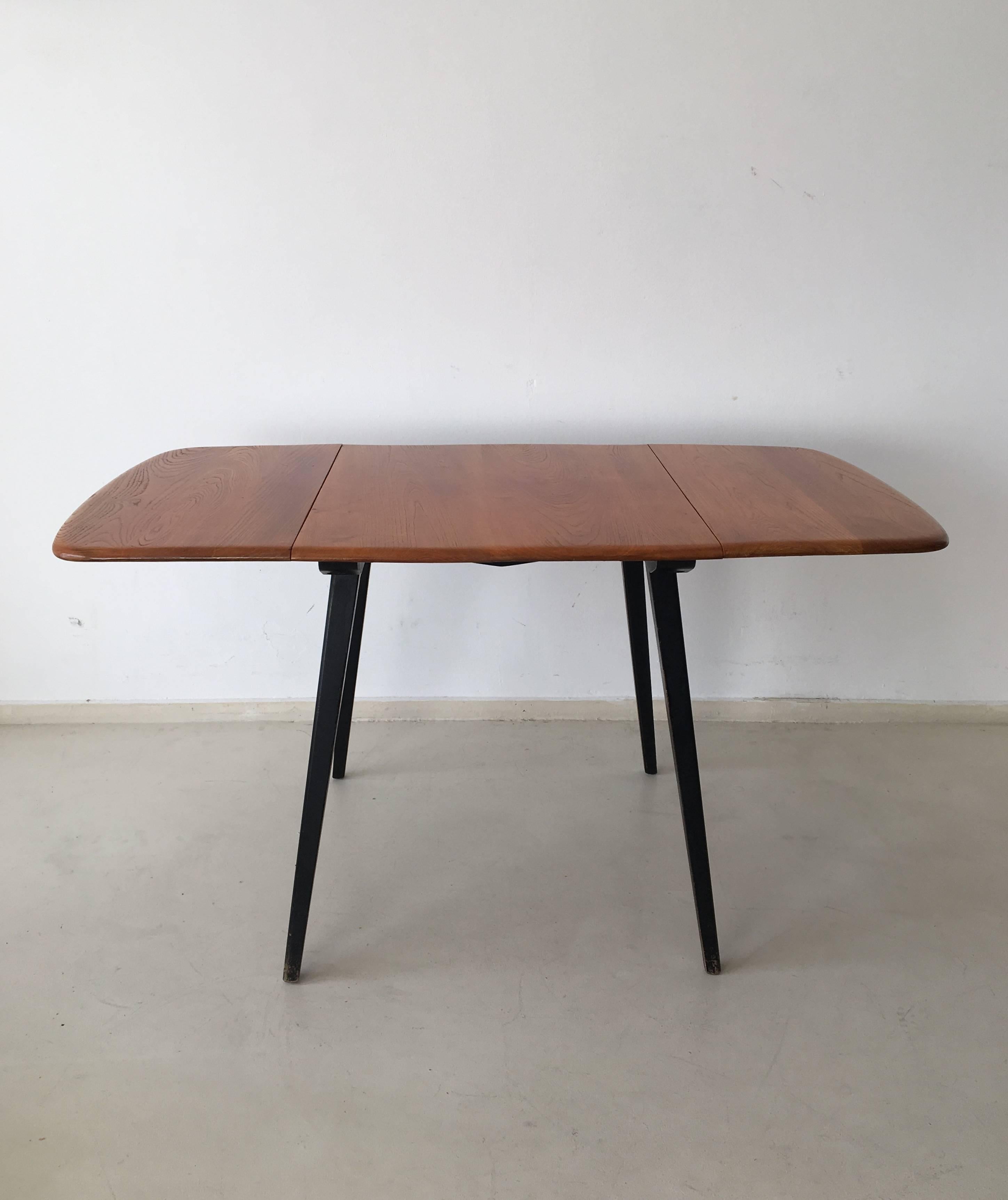 This rectangle double drop-leaf table consists of a blond finished solid elmwood top on tapered black lacquered beech legs. It was designed by Lucian R Ercolani and manufactured by Ercol England in the 1960s. The table is in a very good condition