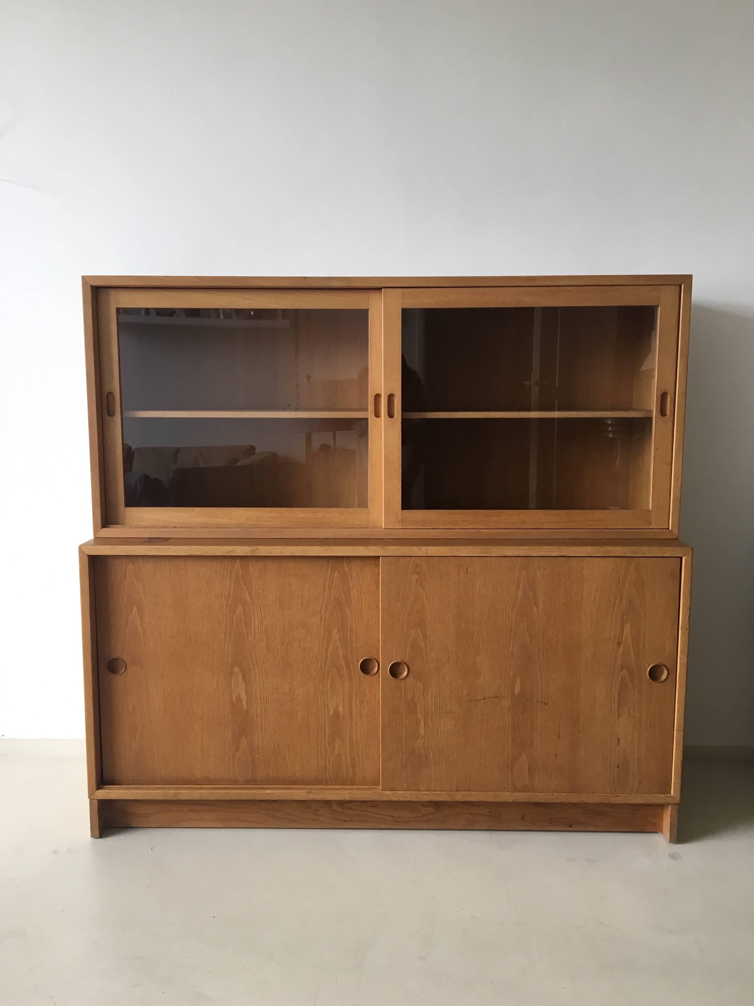 This wonderful cabinet was designed by Børge Mogensen in the 1950s. Both, the virtine part and the cabinet, have sliding doors. This storage is in solid condition with wear consistent with age and use. When the vitrine part is removed for separate