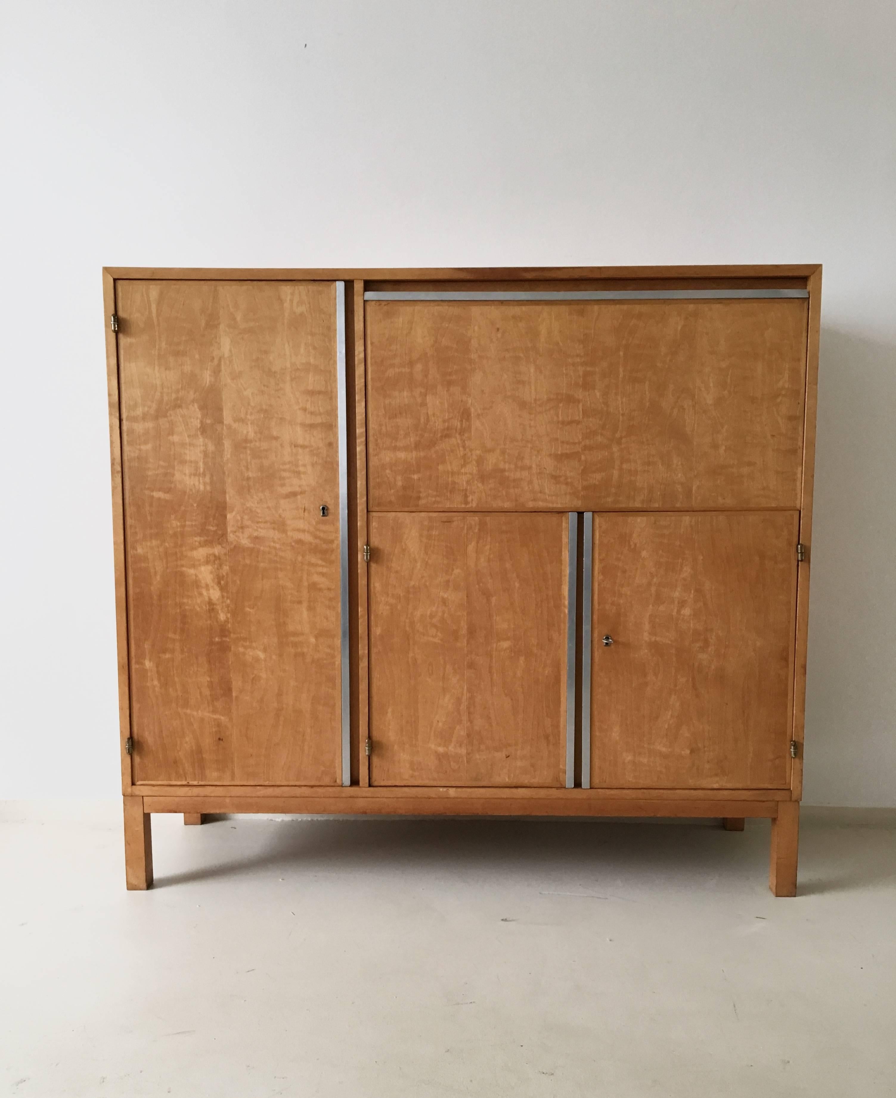 This Dutch Mid-Century cabinet or cupboard originates from the 1950s and was attributed to Cees Braakman for UMS Pastoe. It is made from birch veneer and features shelving space as well as three drawers inside. Some have the typical white lacquered