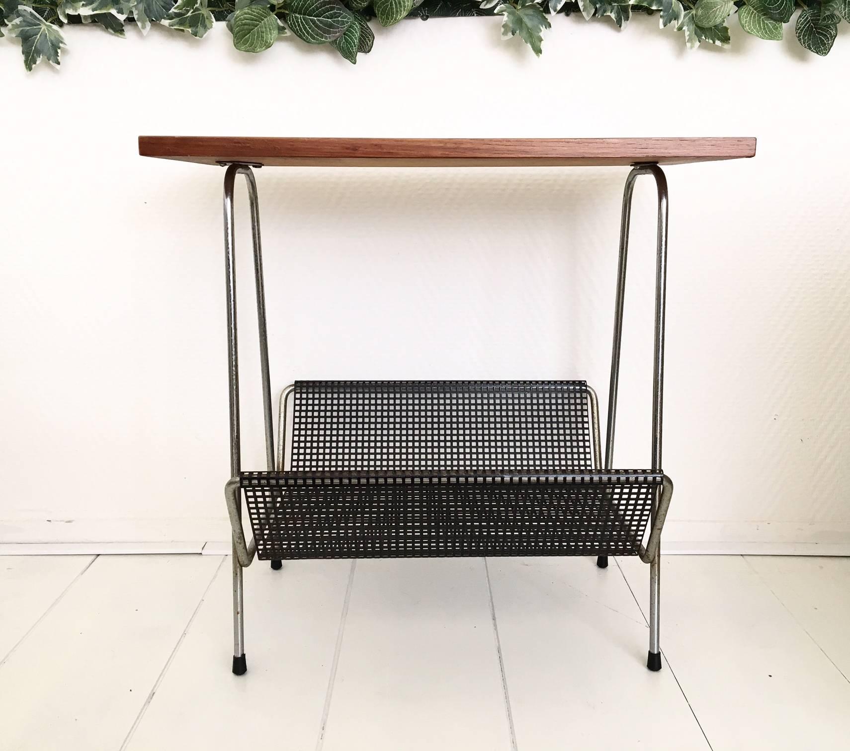 This elegant magazine rack was most likely manufactured by Pilastro circa 1950s-1960s in The Netherlands. It features a Teak top and a black perforated metal basket. Although it shows some oxidation to it's frame, it remains in wonderful solid