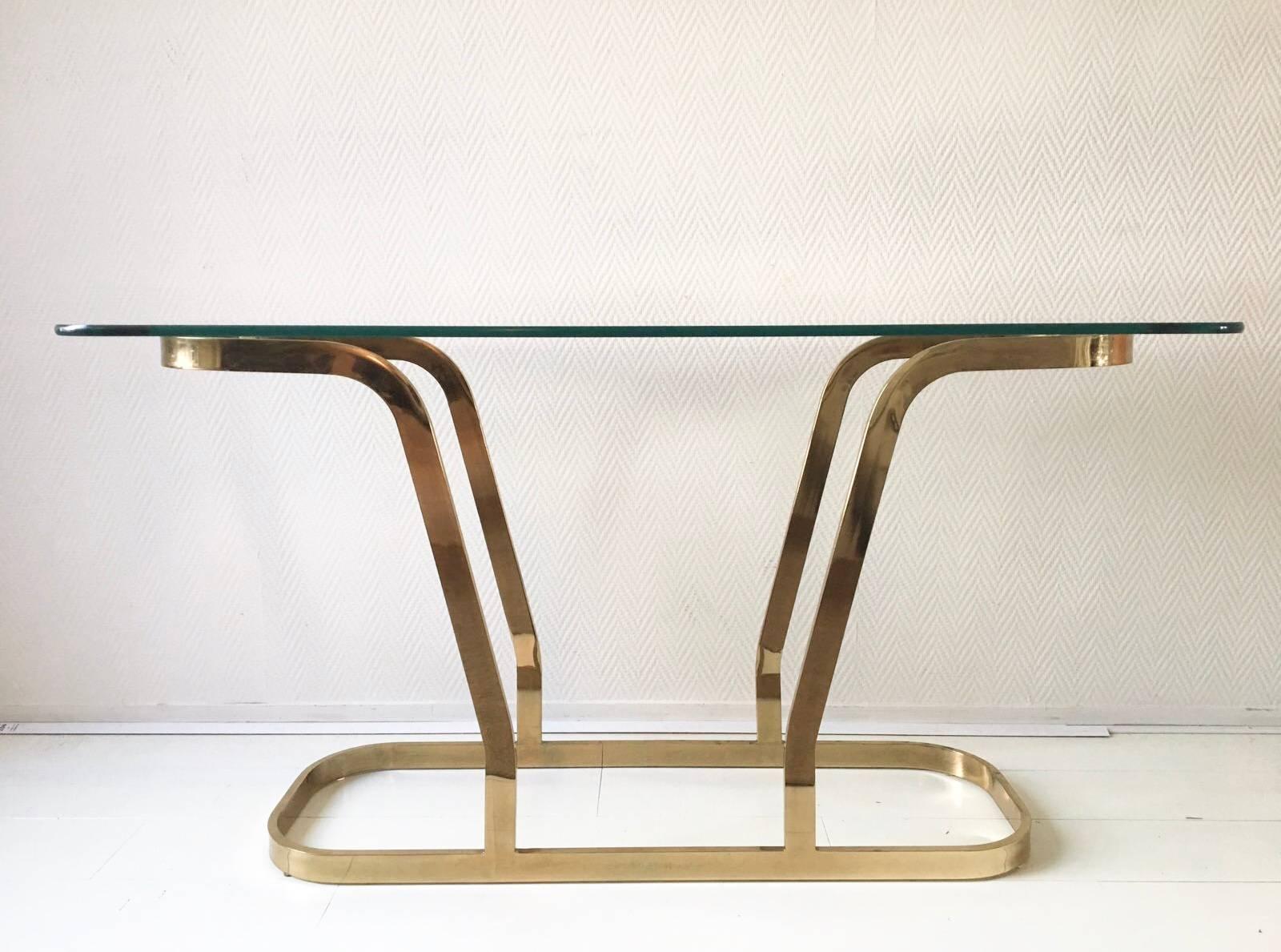 This glamorous console table features a oval shaped thick glass top and a brass colored base. Fabulous in a modern, Hollywood Regency or Midcentury space.

Remains in a good vintage condition with slight traces of age and use.