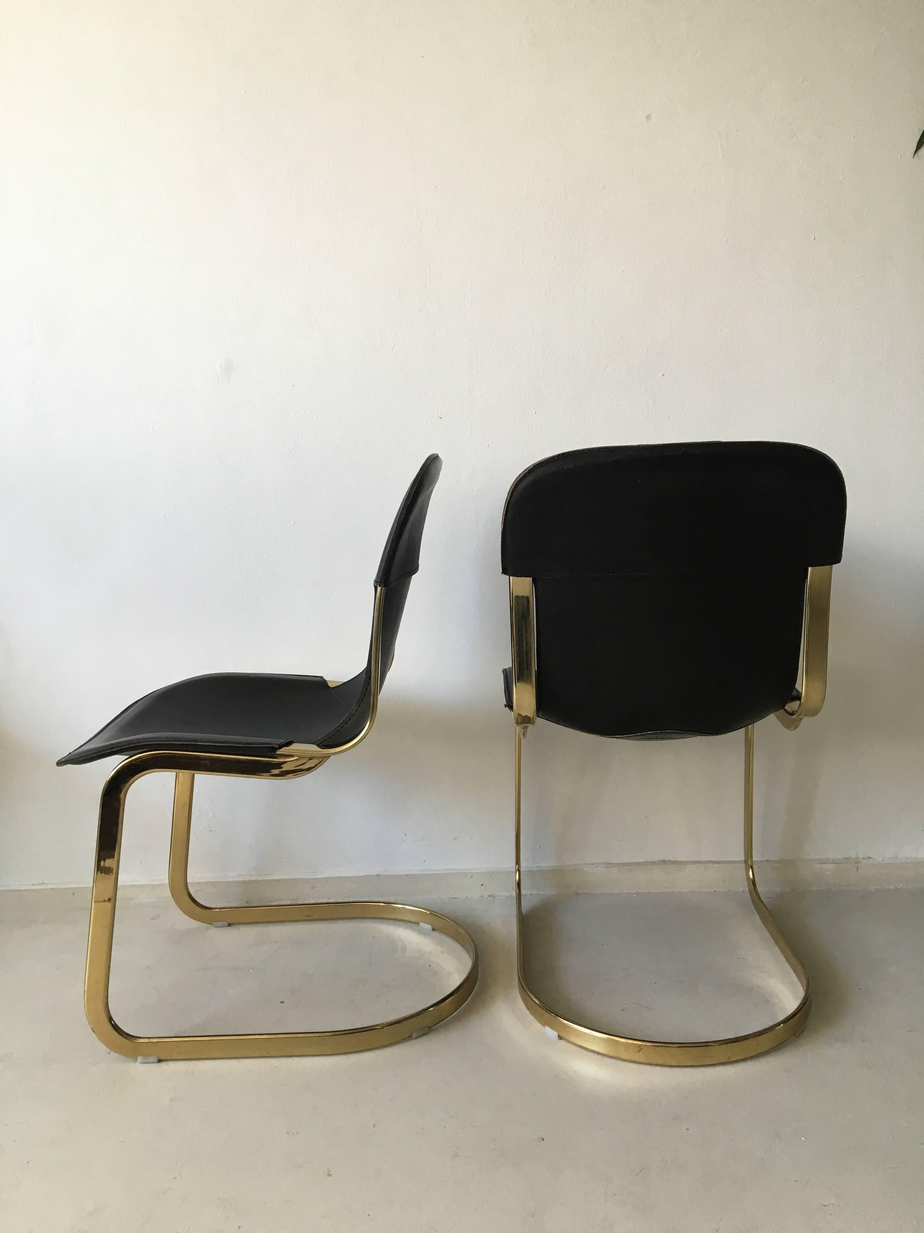 This set of two dining chairs were designed by Willy Rizzo for Cidue in the 1960s. This duo consists of a brass frame and a thick, dark brown leather upholstery. The chairs remain in a very good vintage condition with minor wear.