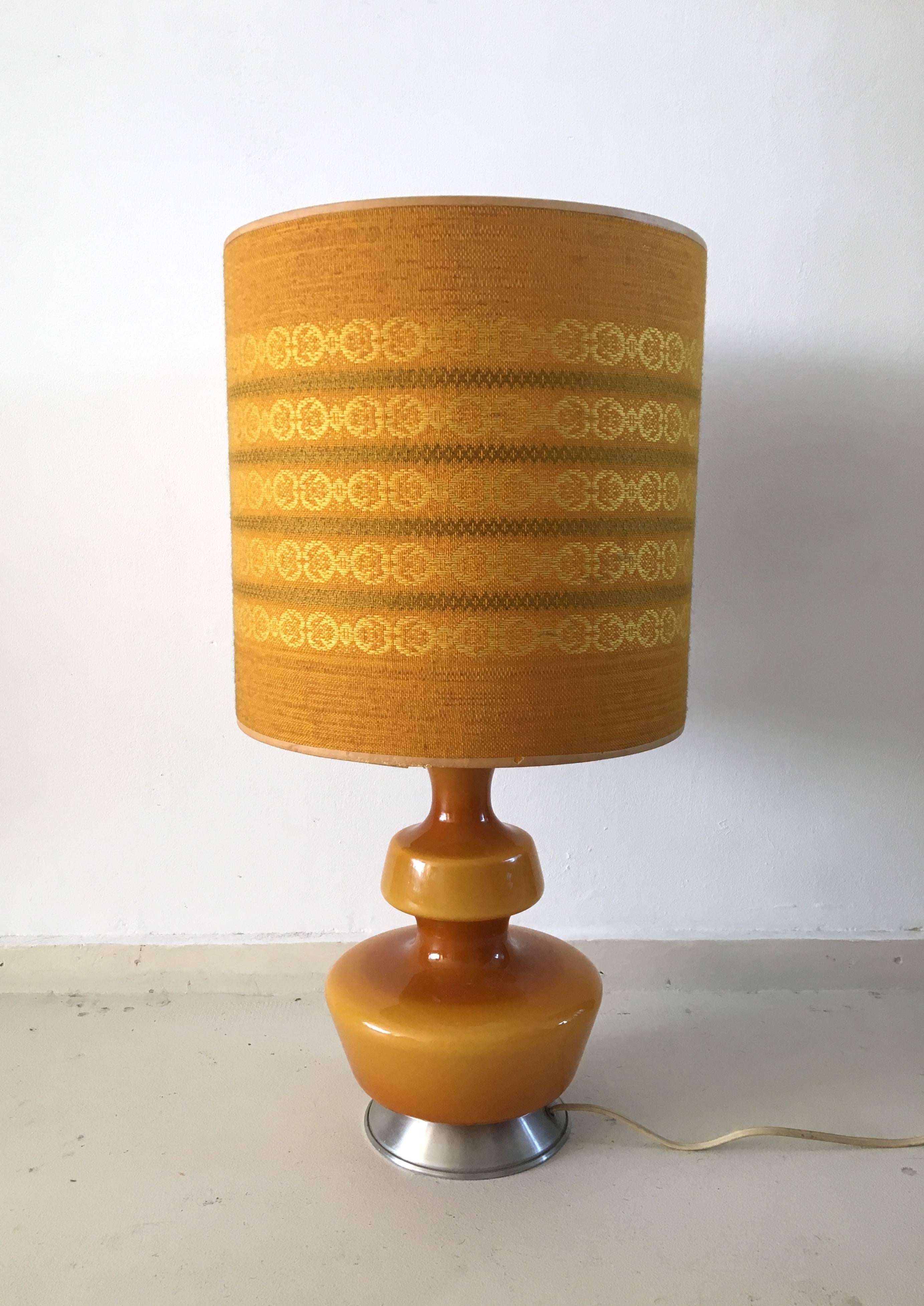 This well preserved, vintage lamp was designed and manufactured by Holmegaard, circa 1960s. It features an ochre or brown foot in glass with a metal base and the original shade with beautiful pattern. Wires also in European original condition. This