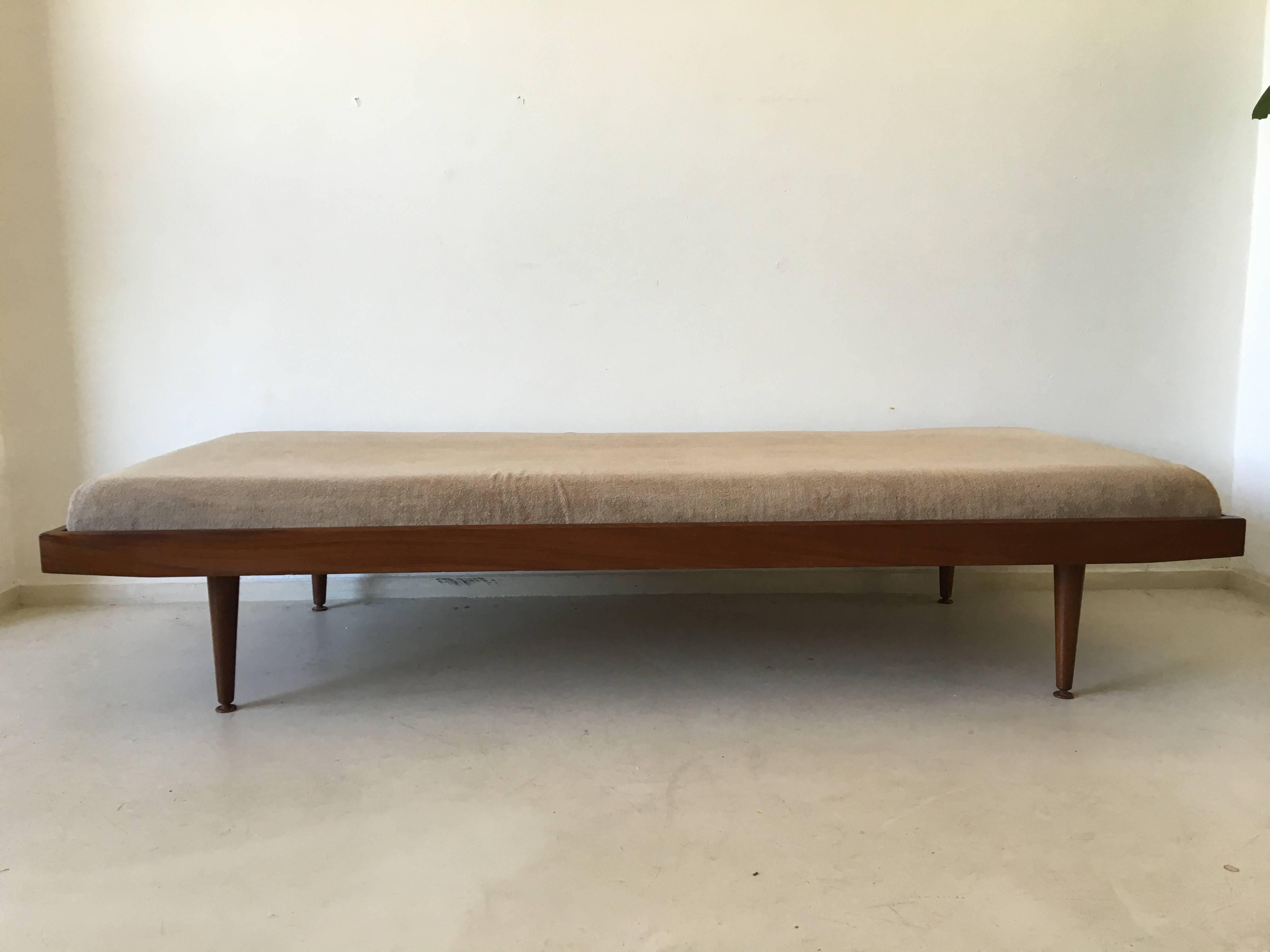 This elegant daybed was designed and manufactured in Europe by most likely Pastoe. It features a teak frame with brass caps and movable feet at the end of the legs and a sand colored mattress. It remains in very good condition with wear consistent