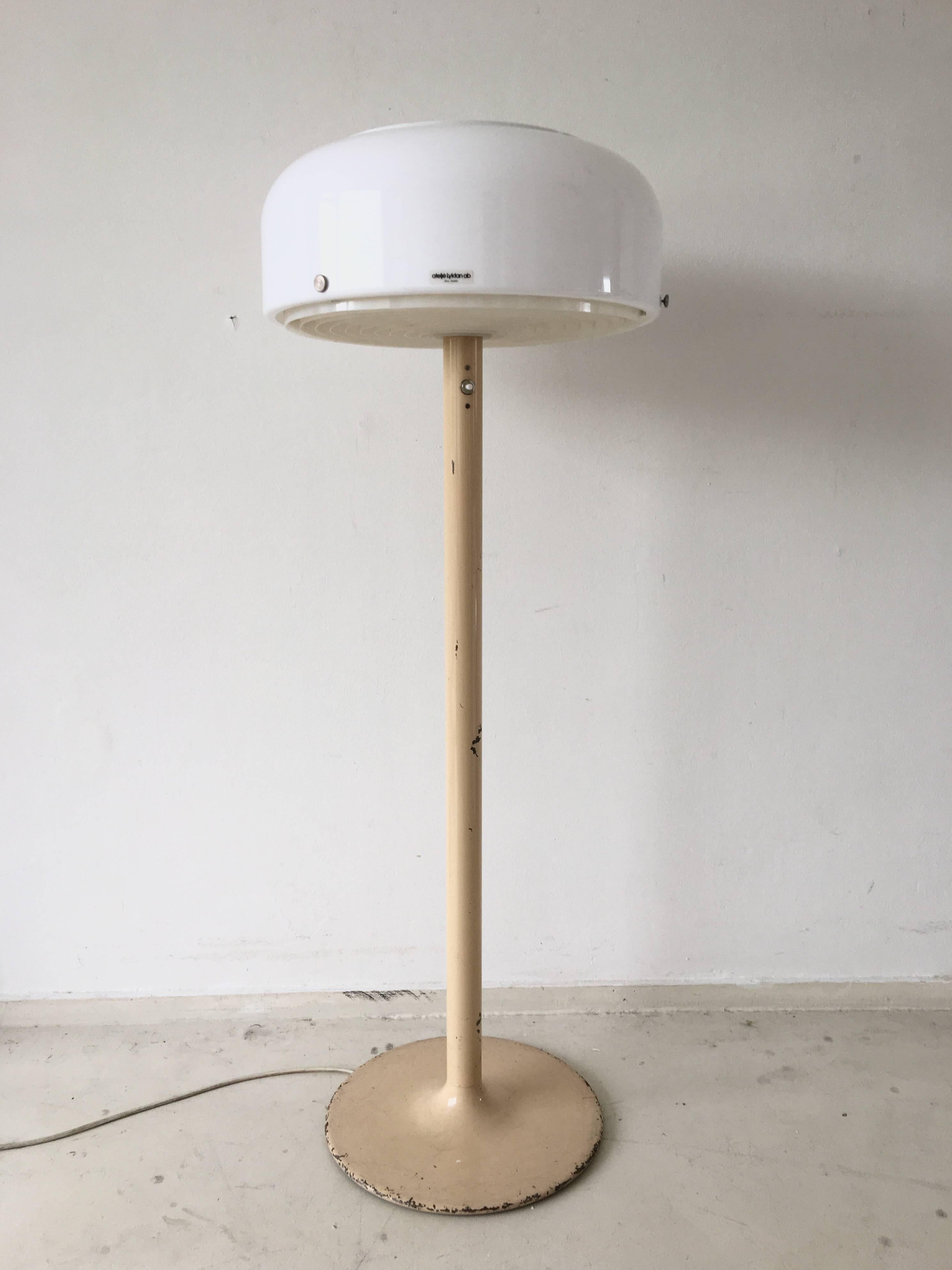 Diese schwedische Industrial-Stehlampe wurde von Anders Pehrson um 1970 herum entworfen. Sie hat einen cremefarbenen Metallsockel und einen weißen Acrylschirm. Im Inneren des Schirms sorgt ein Kunststoffring für eine gute Verteilung des Lichts.
Die