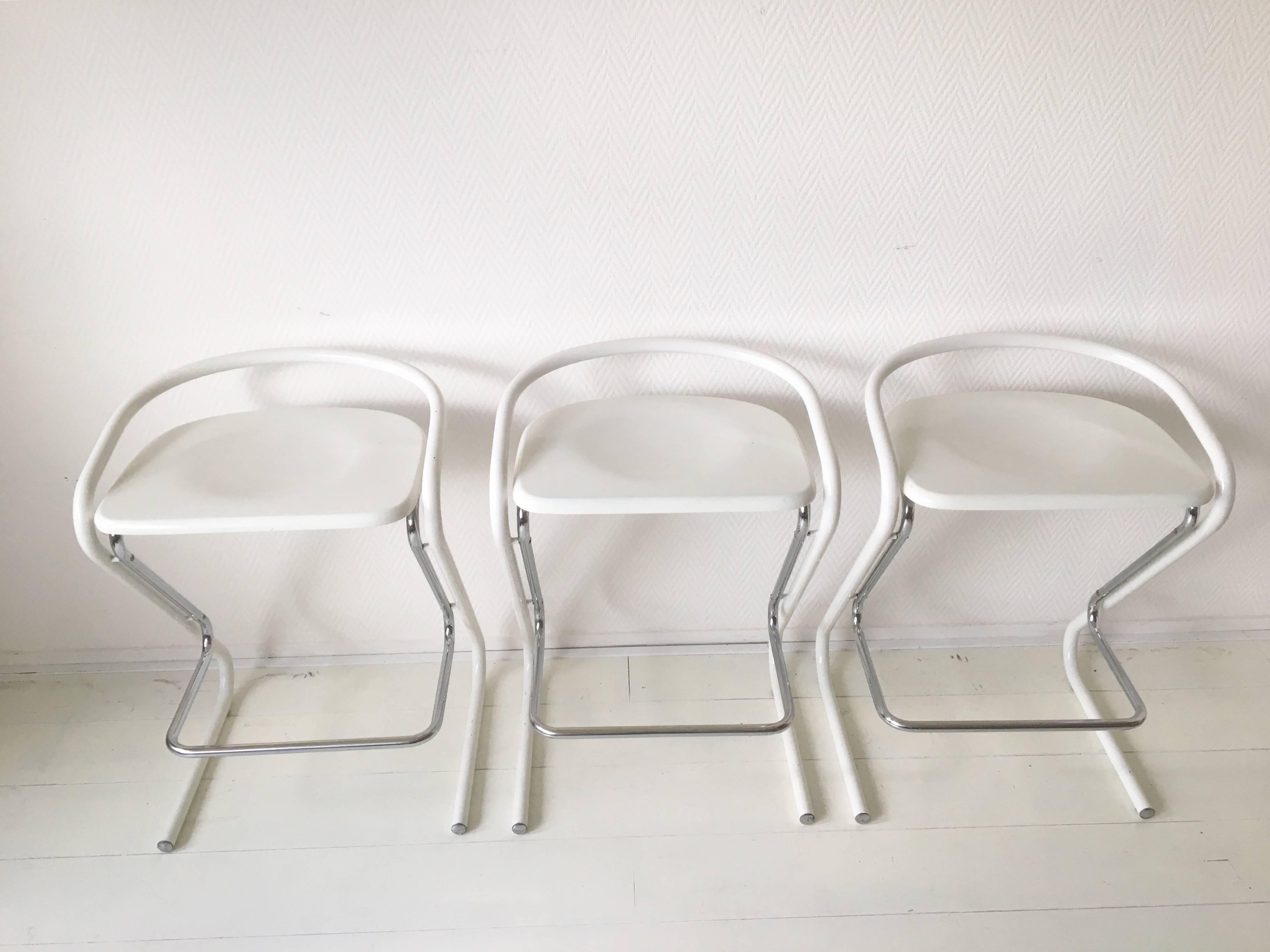 This wonderful set of three feature a white and chromed metal base with comfortable seatings of wood. They were designed and manufactured in Italy. The stools remain in good vintage condition, with some signs of age and use. Marked with the