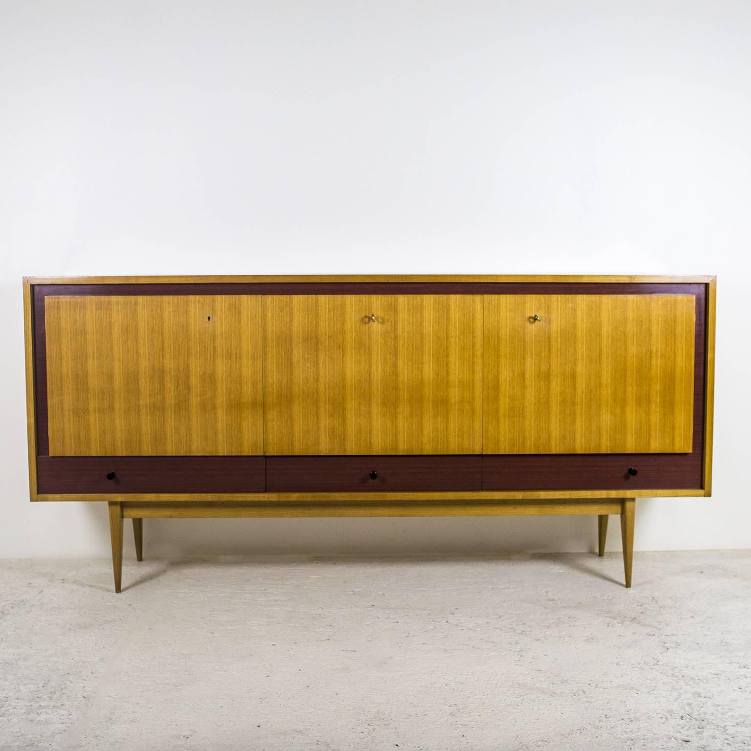 A 1950s sideboard by the French designer Charles Ramos. The frame is in light ash wood outlined by brown laminate to create a beautiful contrast. The piece of furniture, resting on four sabre legs, is made of two opening doors on the sides, a