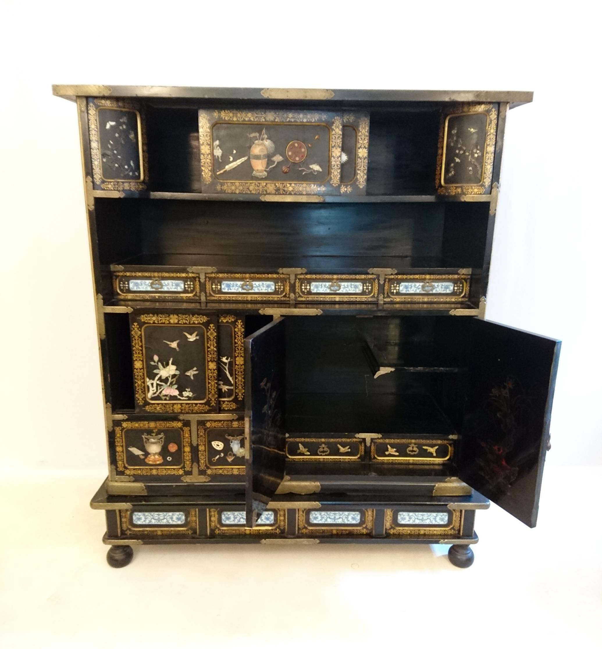 This Japanese Shibayama guilded cabinet from the Japanese Meiji period with cabinets, doors and shelves. With decor depicting animals and various instruments in bronze, porcelain, mother of pearl, bone etc. The two largest doors have decor of