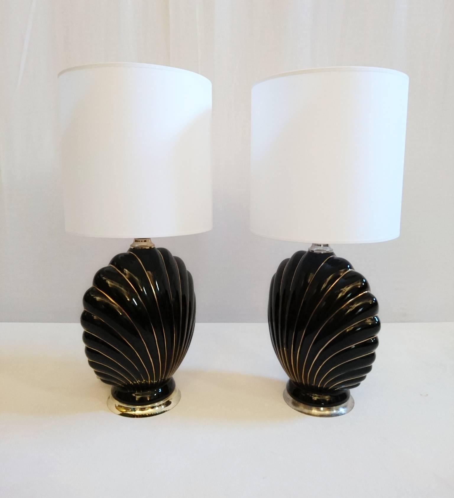 A pair of matching coquille table lamps in black porcelain with gold stripes. They are similar but not identical on the base. But that´s hardly detectable if they are not standing next to each other. Brand new white lampshades.