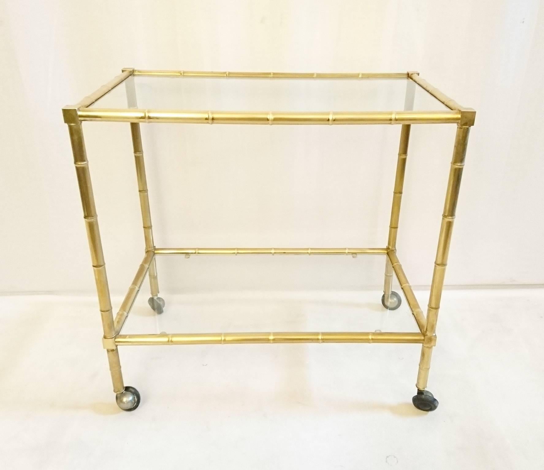 Two-tier bar cart in brass made to look like bamboo. Clear glass and original well working wheels.