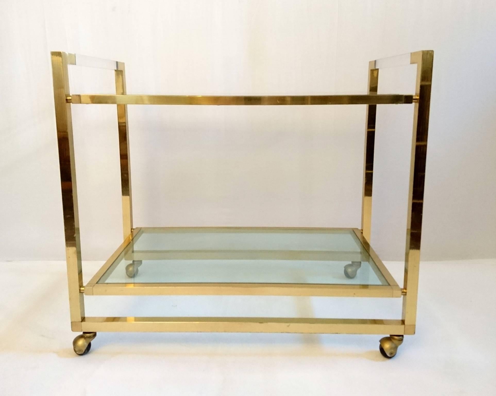 Two-tier bar cart in brass with Lucite handlebars and glass shelves. High quality and solid construction. Original well functioning wheels.