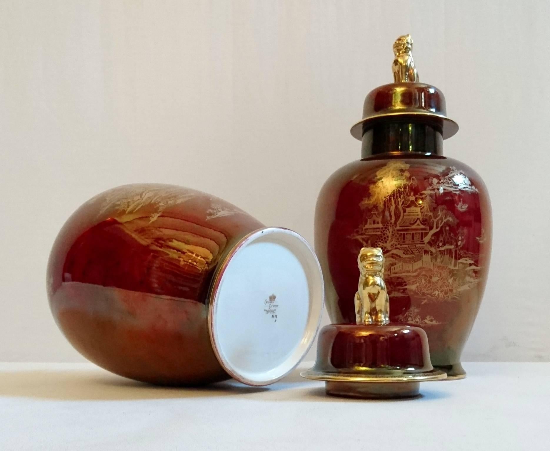Ruby colored pair of lidded porcelain urns by Crown Devon Fieldings with gold chinoiserie motifs. The lids are crowned with lions in gold. Both urns and lids in perfect condition and without chipping or fading. Stamped in the base and numbered.