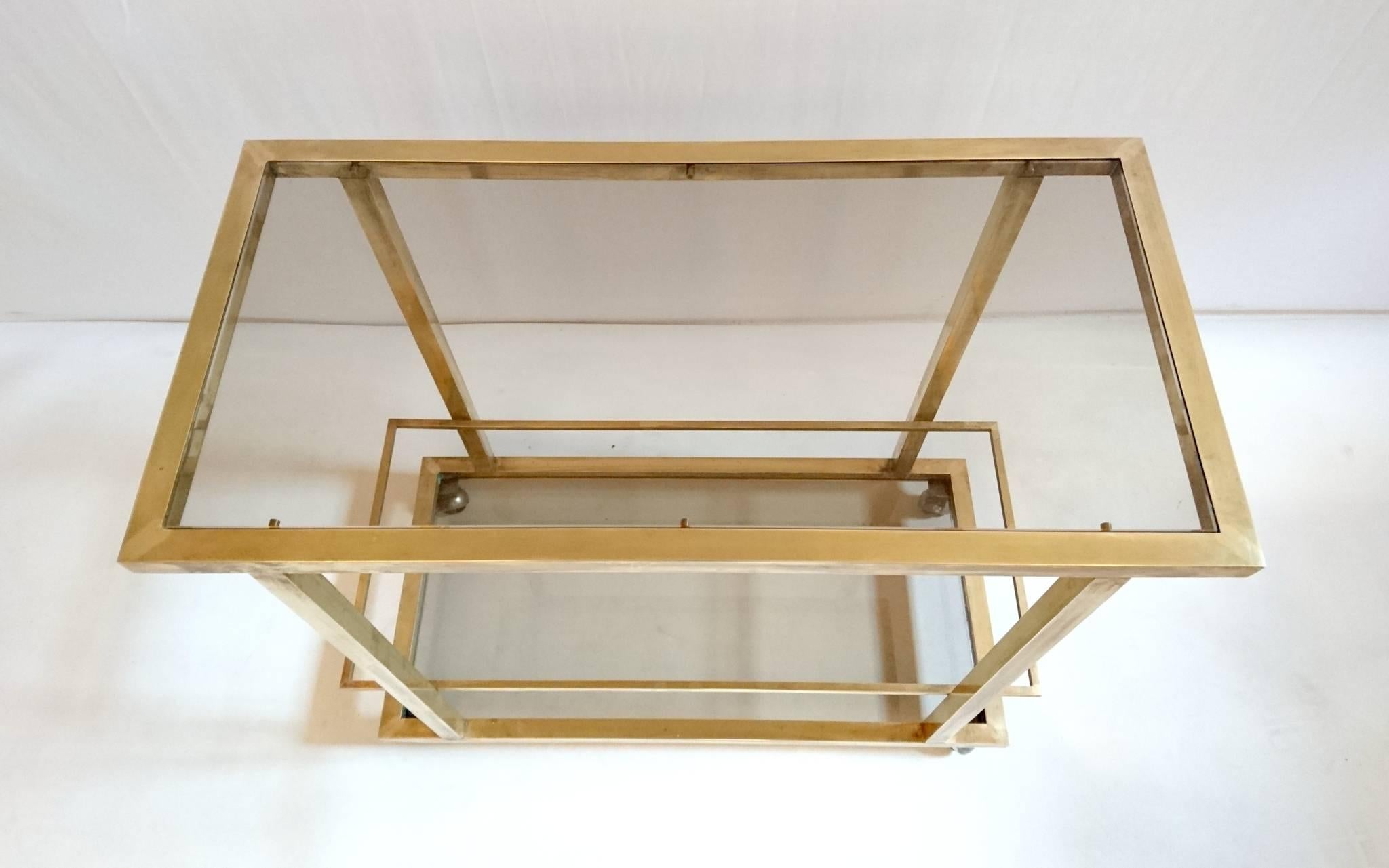 Two-tiered bar trolley in brass with smoke colored glass. The lower level is made for bottle with a brass rim keeping them from falling off.