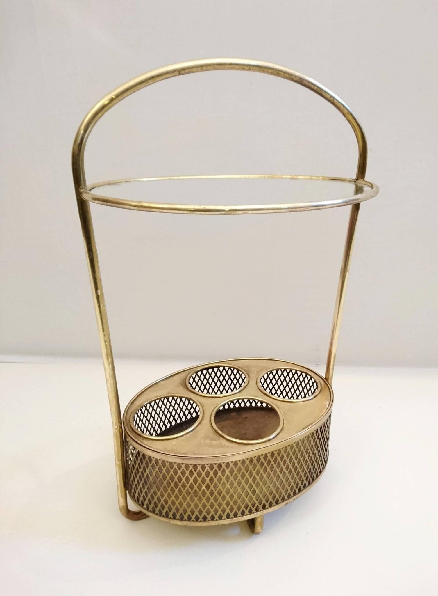 Unusual portable table in brass with a clear glass tabletop. Featuring a holder for four bottles at the bottom surrounded by a mesh in brass.