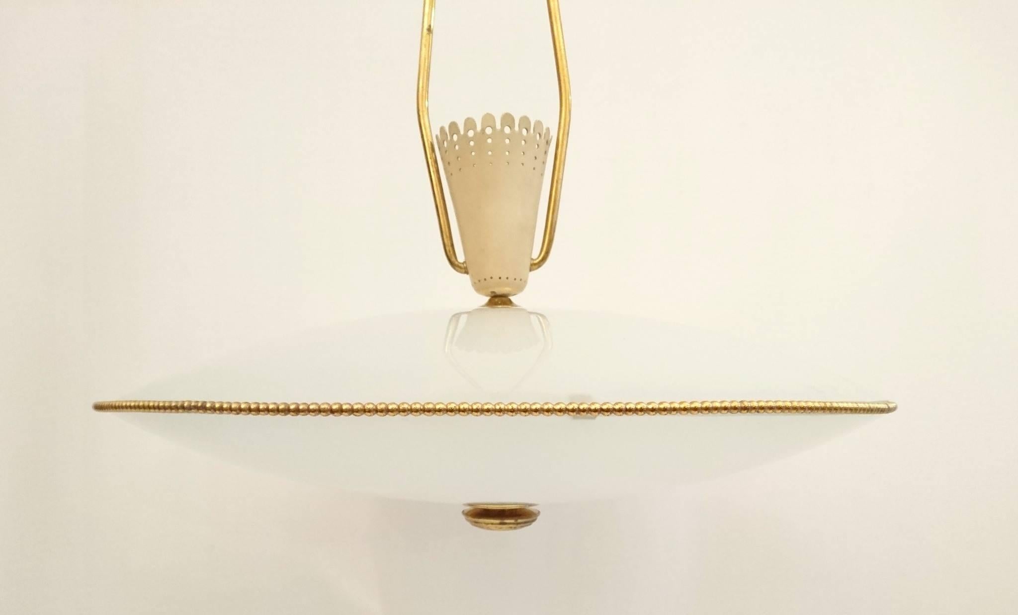 Disc pendant with milky white glass surrounded by a pearl border in brass. As well as having light inside the disc there is uplight inside the ivory colored cup on top.