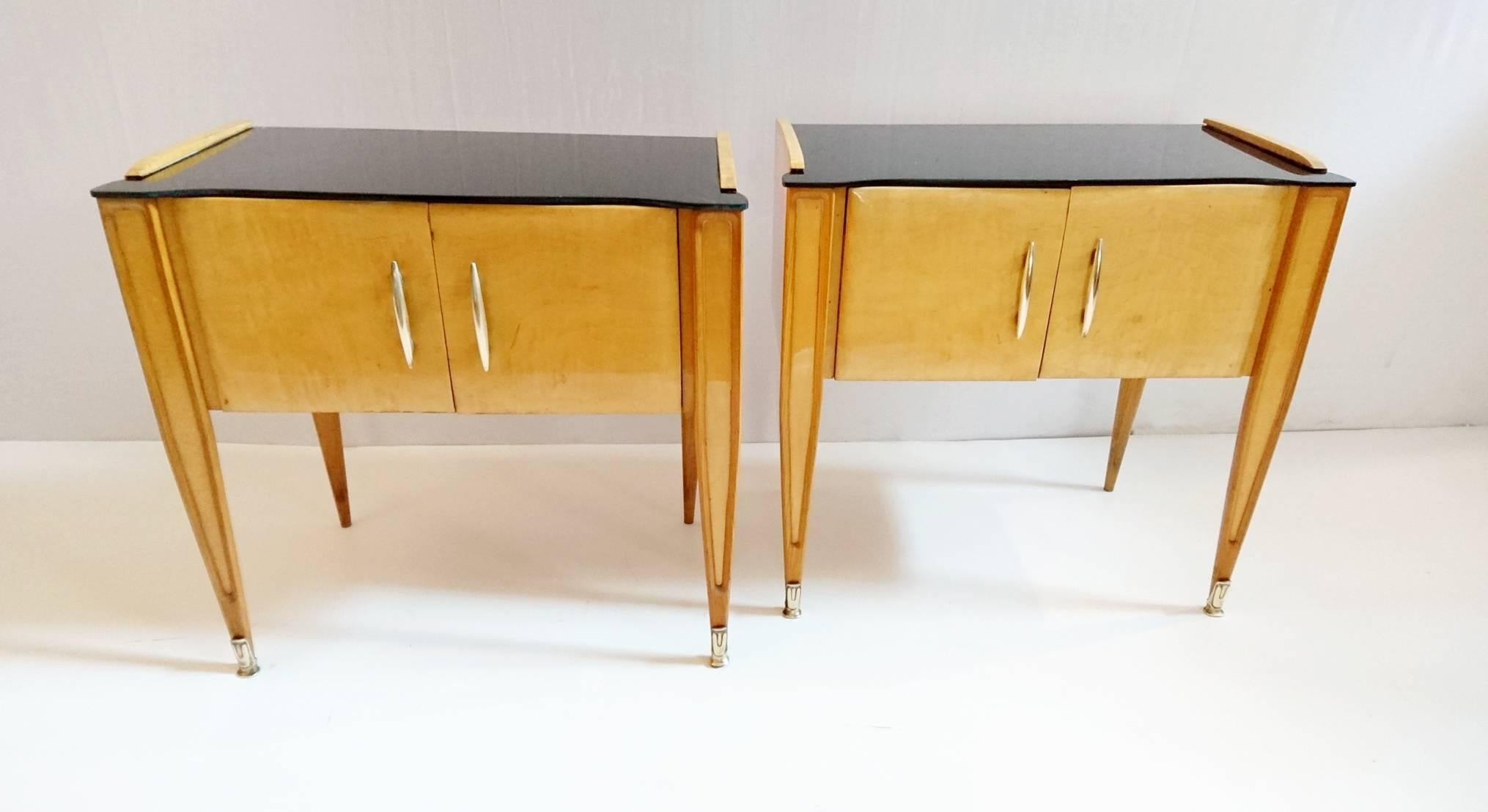 Nightstands with double doors with curved brass handles, standing on slim tapered legs with custom brass endings, each table glass is black on top surface. Before delivery both tables will be professionally restored.