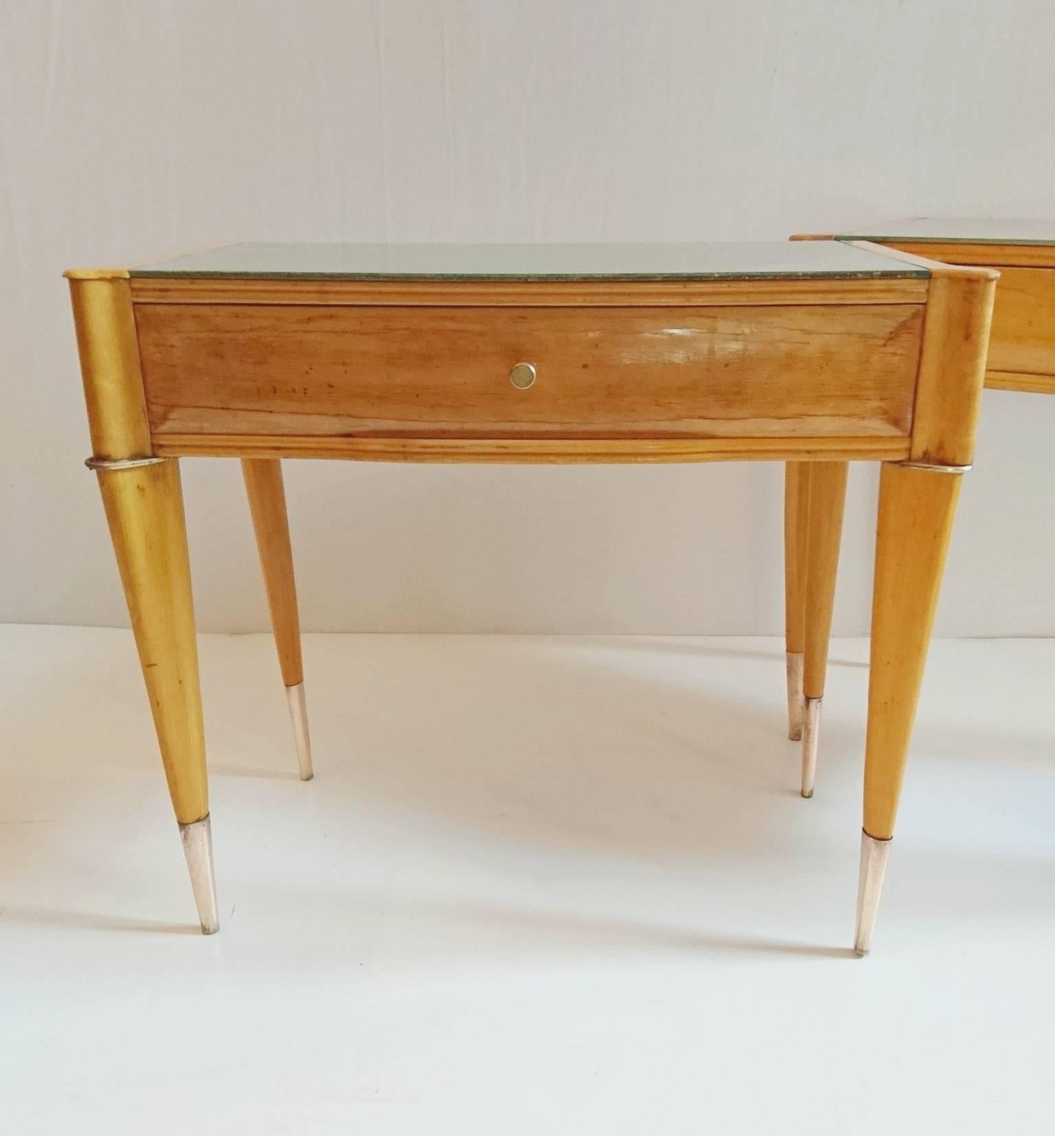 Elegantly shaped blond nightstands in maple and birhch with slightly silver/greenish glass tops with brass details. Has cone shaped delicate legs with brass finishes. Will be delivered professionally restored and polished upon sale.