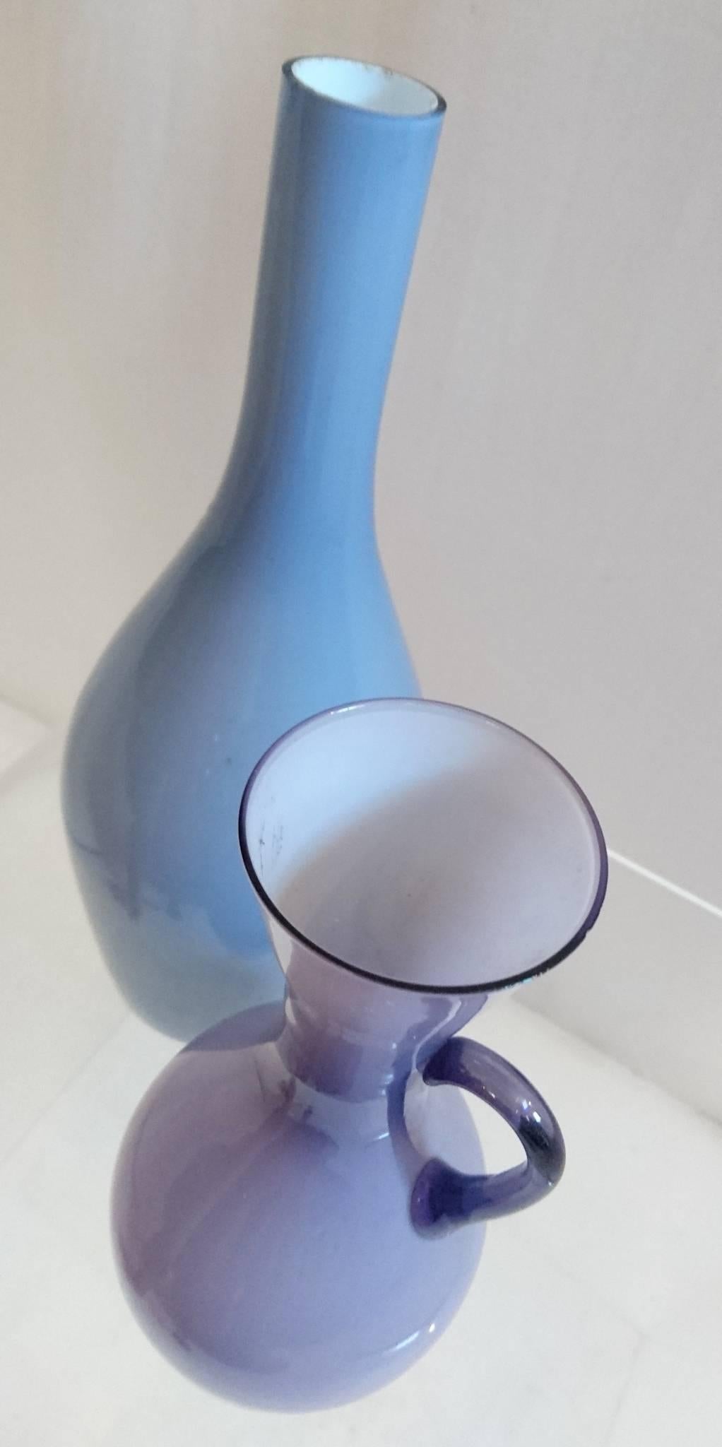 Two vases by Swedish glass manufacturer Ekenäs (now defunct) in two shades of purple opaline glass with white insides. One has a handle on the side.
Measure: The larger is 29 cm high and 10, in diameter and the smaller is 21 cm high and 9 in