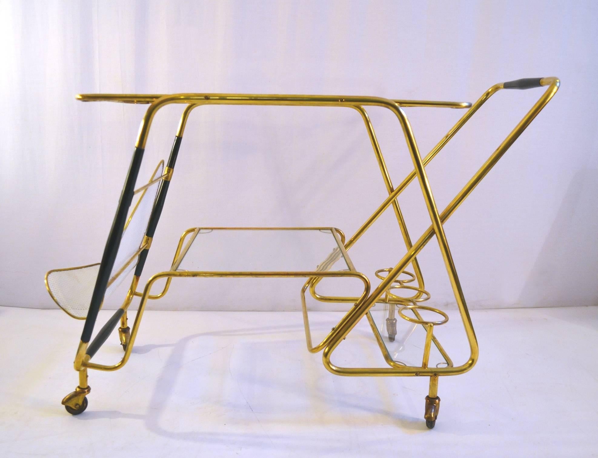 Unusual two-tiered bar cart with bottle holder as well as a magazine rack by Cesare Lacca, Italy, Made in brass and stained wood with clear glass trays. In excellent condition with wheels in good condition. Wood is restored and the brass polished.