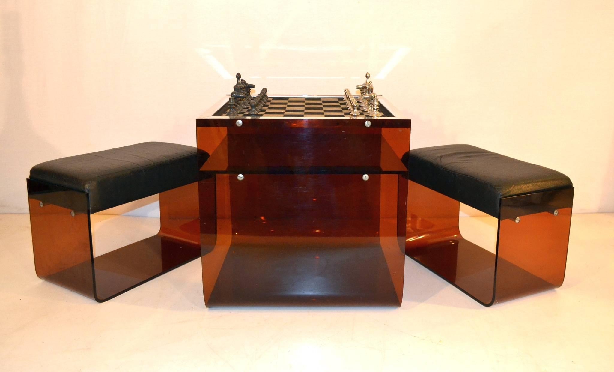 Unusual chess table made from brown plexiglass with a pair of stools with faux leather seating. The chess pieces are solid metal in chrome and gray and  chess board in suede. Around the chess board there is a rim in aluminium. There is also a piece