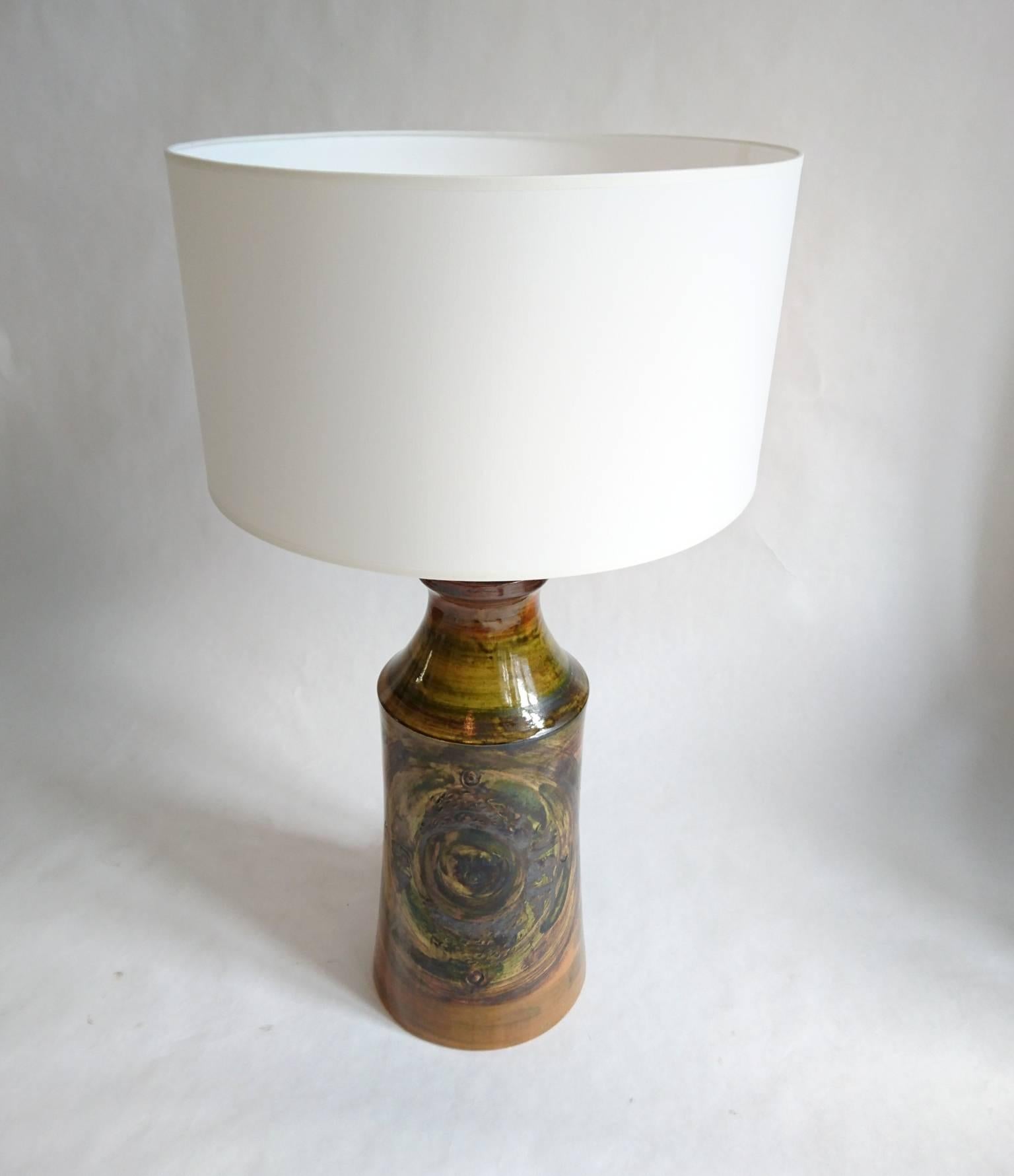 This Swedish handmade ceramic table lamp which is not only fantastic but also cool and striking. Has a multicolored hand-painted decor in browns, greens and black. Comes with a brand new drum shade in cotton. Electricity is functioning.