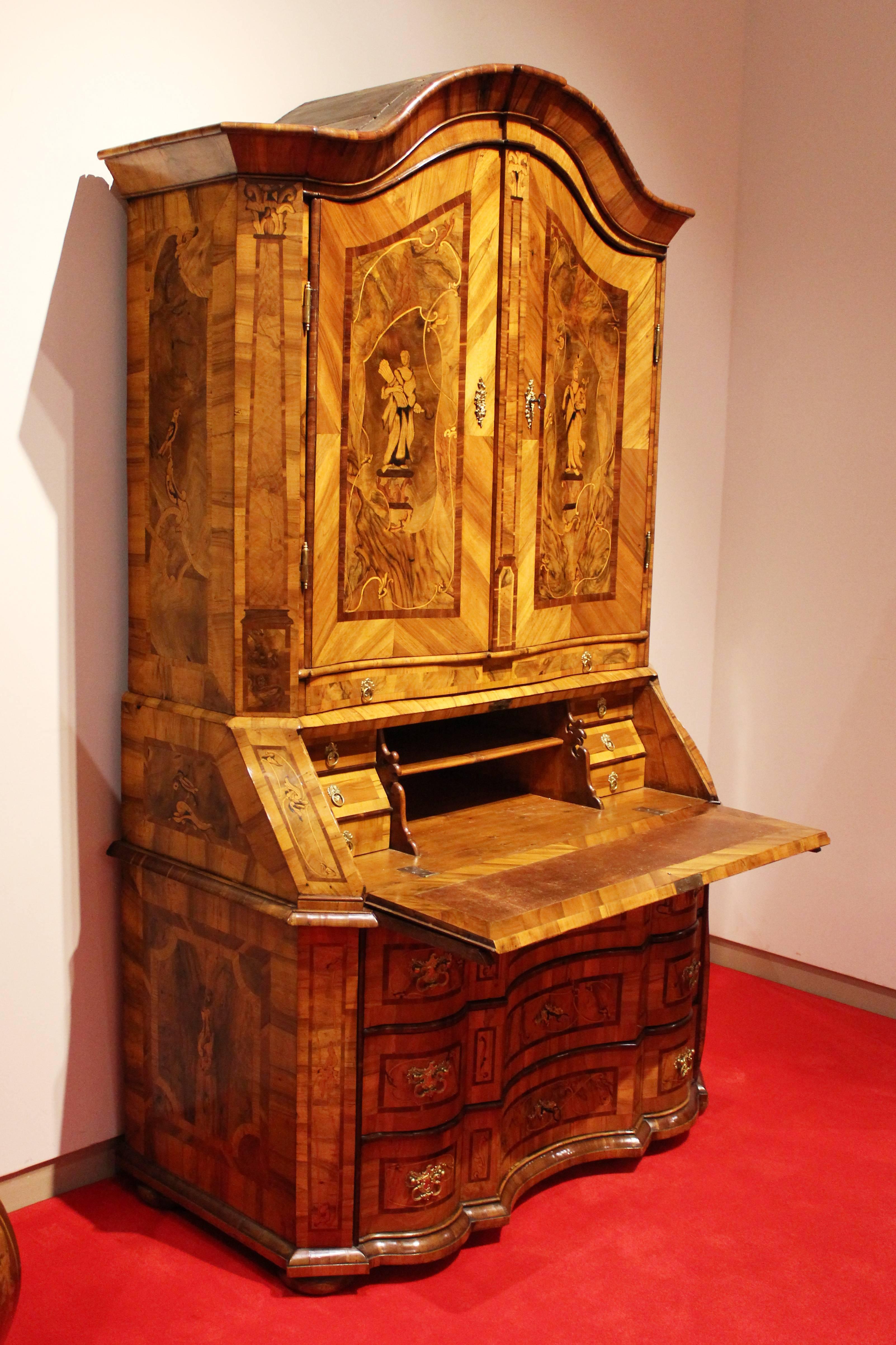 Walnut-tree and walnut-tree root on softwood body.
Several times curved drag.
Six drawers behind the writing record.
Bulged out upper top with two doors and 12 small drawers and shelf
Rich figurale and florale inlaid works. 
Four Seasons are