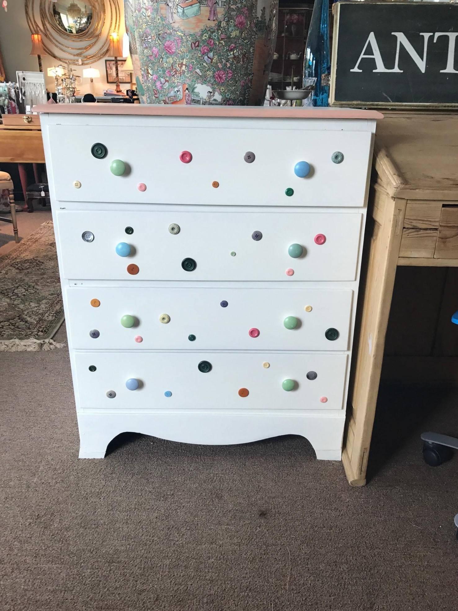 Cute as a button - button dresser with pink perimeter, white top, baby blue draw pulls dovetailed. Wonderfully old and made by a local artist multicolored buttons attached for charm. Four great drawers - solid wood structure painted a decorator's