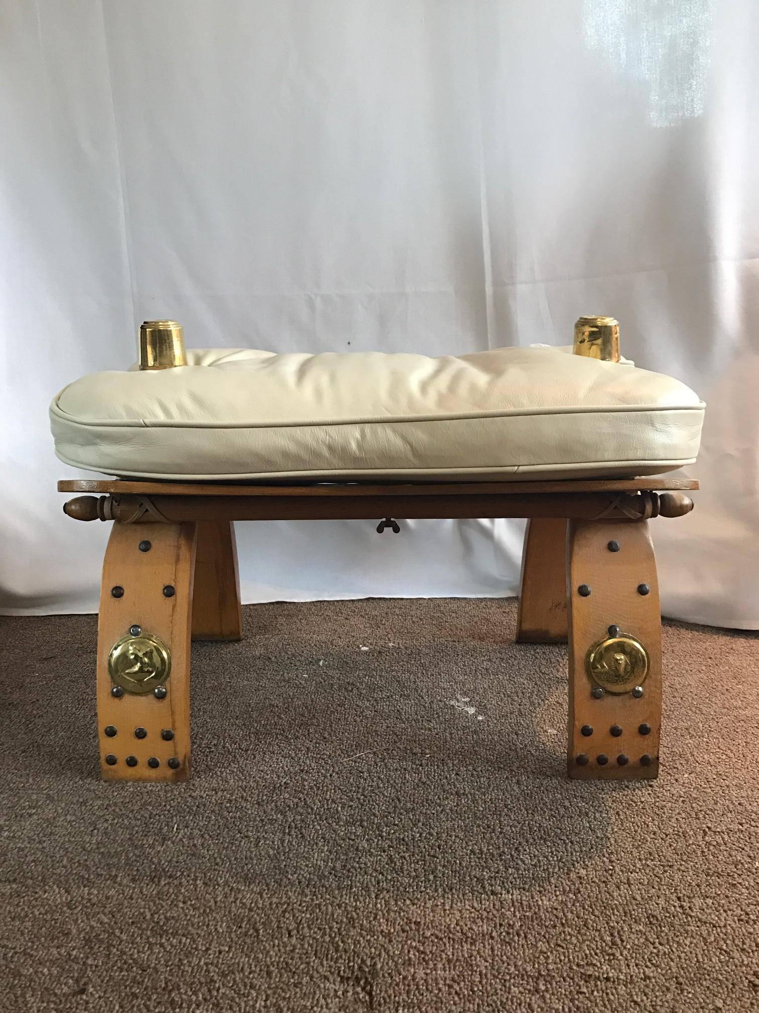 Unique Egyptian camel bench or ottoman. Creme colored soft supple leather seat wood frame with gilt gold medallions. Seat height 13.5 inches.
