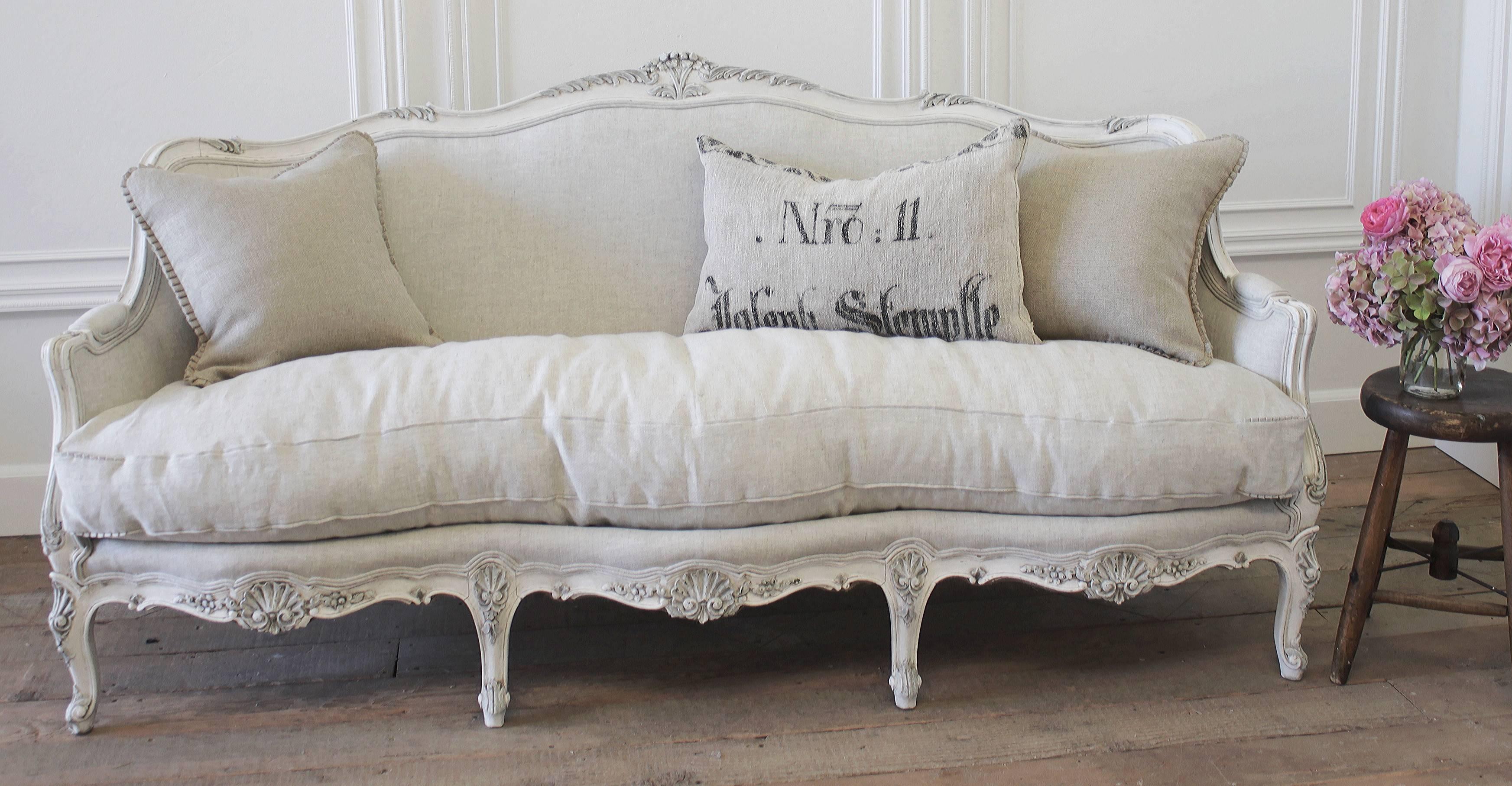 Beautiful antique sofa with carved flowers and shell motifs, painted in our signature oyster white finish and reupholstered in a heavy Belgian Linen. The sofa frame has a two tone painted finish, all of the carvings are hand-painted in a soft French