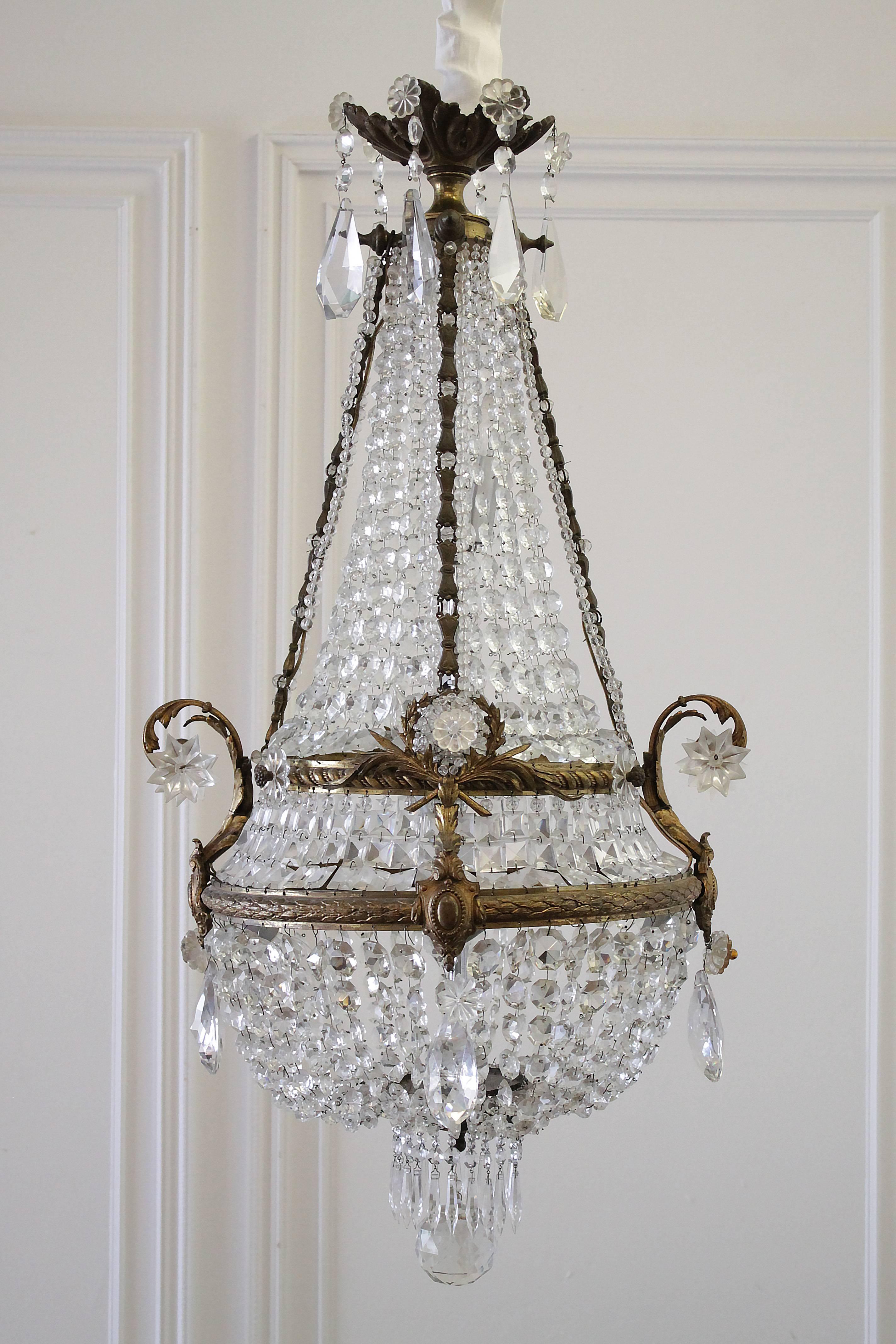 French gilt bronze and crystal seven-light basket chandelier with decorative gilt shields, laurel wreath, graduated cascading bell flowers, and terminating with icicle shaped crystals, and large sphere.
Measures: 39