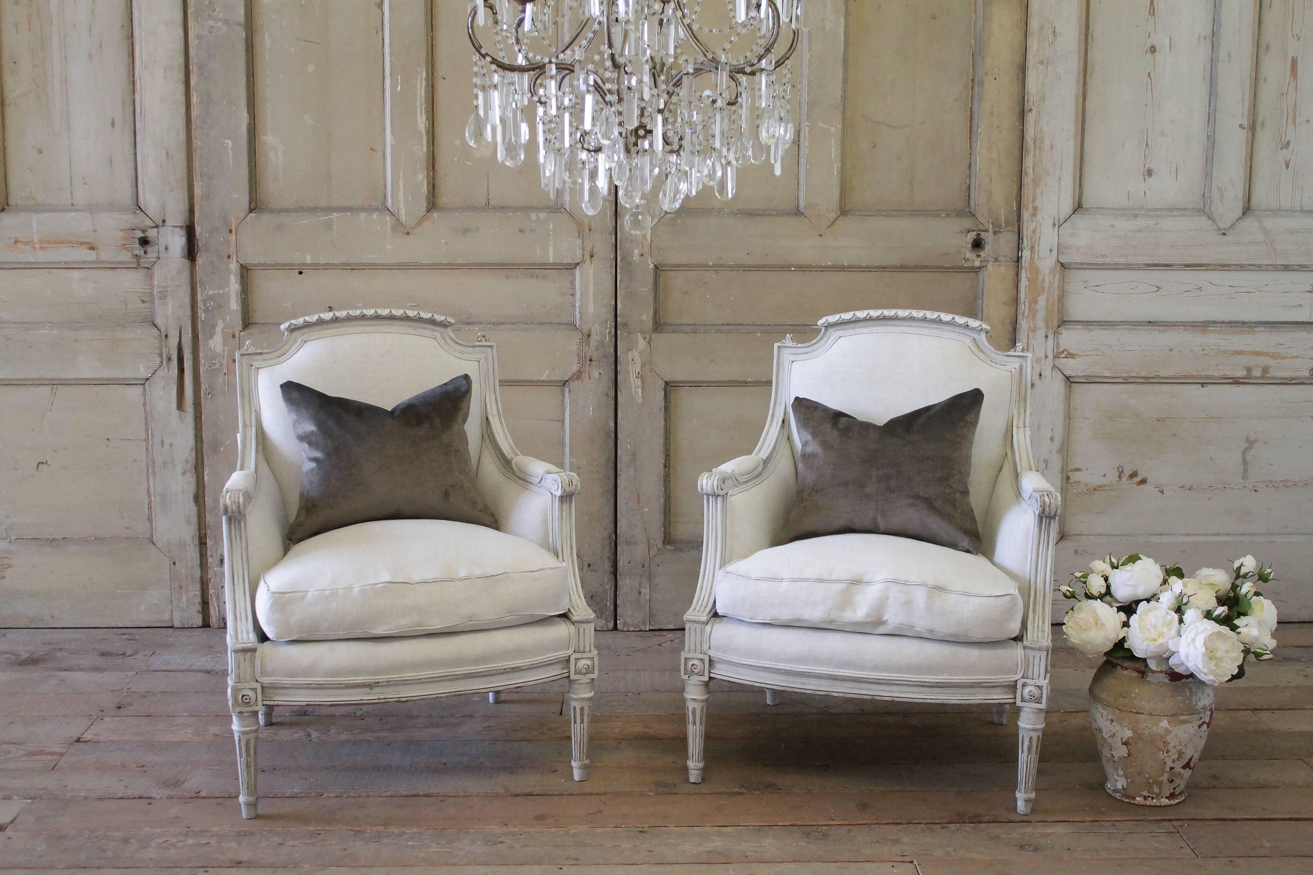 Lovely pair of chairs have been repainted in our signature oyster white finish. We subtly distress the edges and hand glaze the finish to give it an antique patina. Our reupholstery has been done in a light natural Belgian linen, finished with a