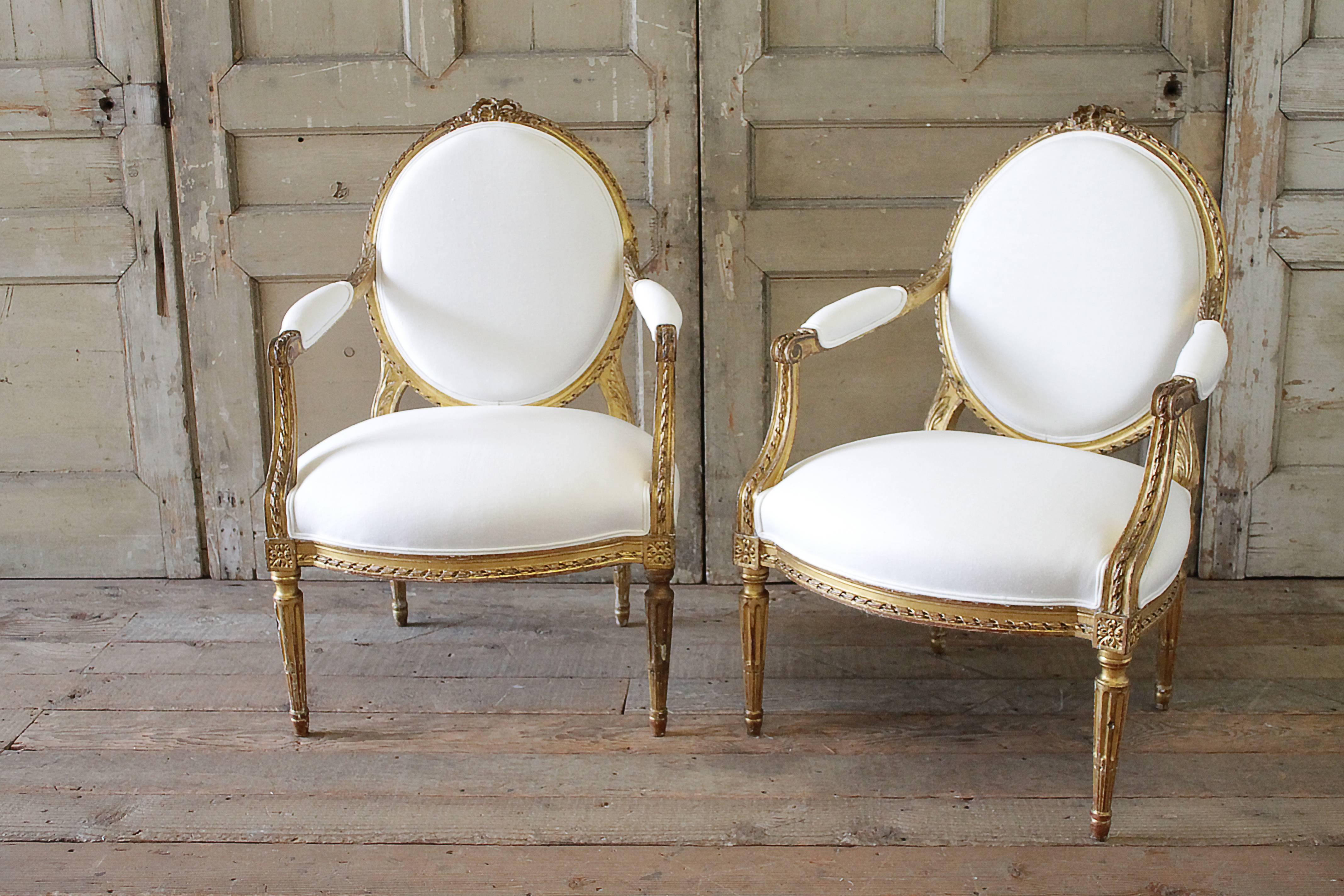 Beautiful larger size arm chairs with ribbon carved crest. Original finish has a wonderful aged patina, gilt has slight distressed edges. We have reupholstered this sofa in our 100% soft white Belgian linen. Linen has been prewashed and has a soft