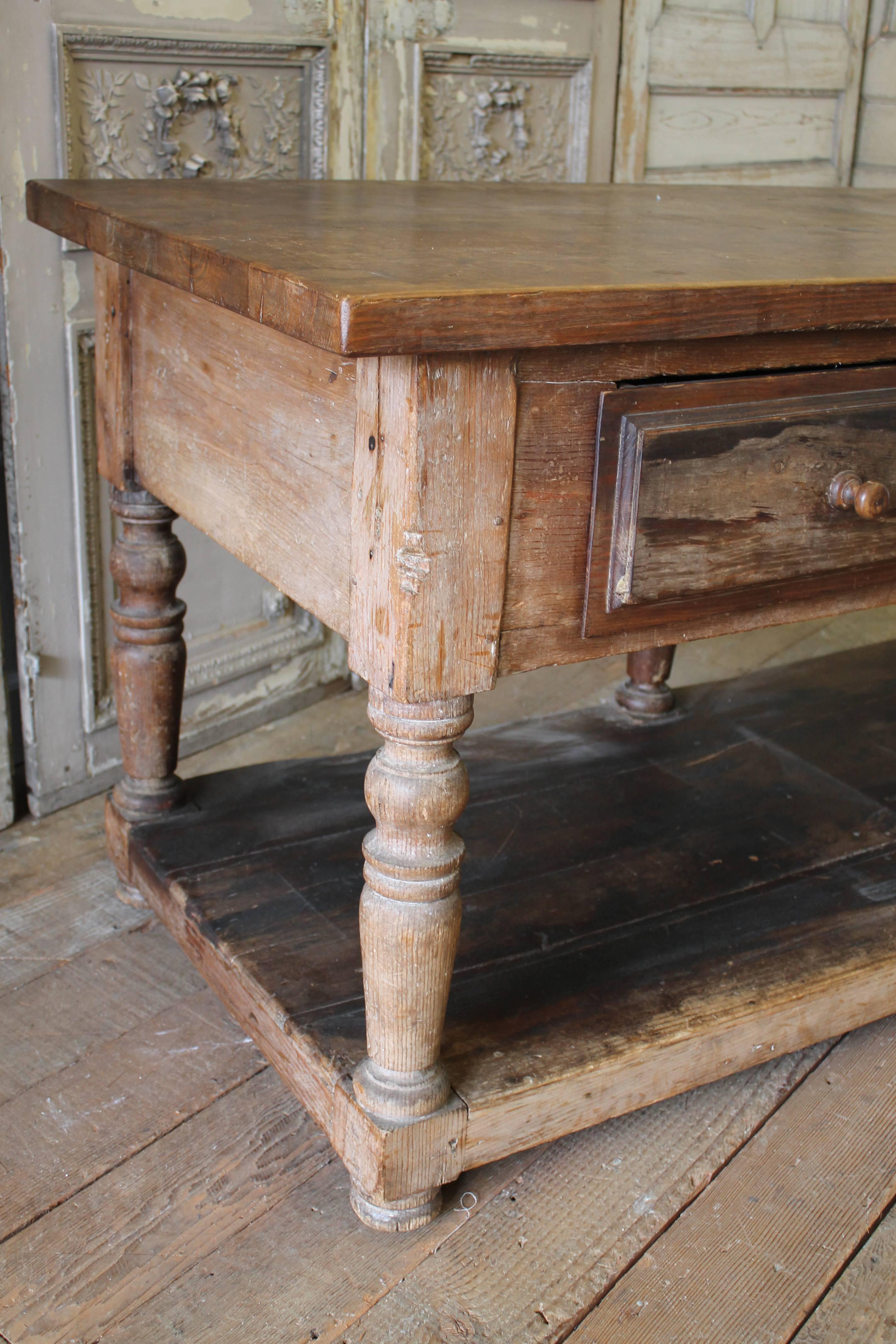 Well loved antique drapers table with weathered patina. This antique French drapers table ("table de drapier" in French) featuring two drawers on the front and a large second shelf on the bottom and turned legs. These tables were commonly