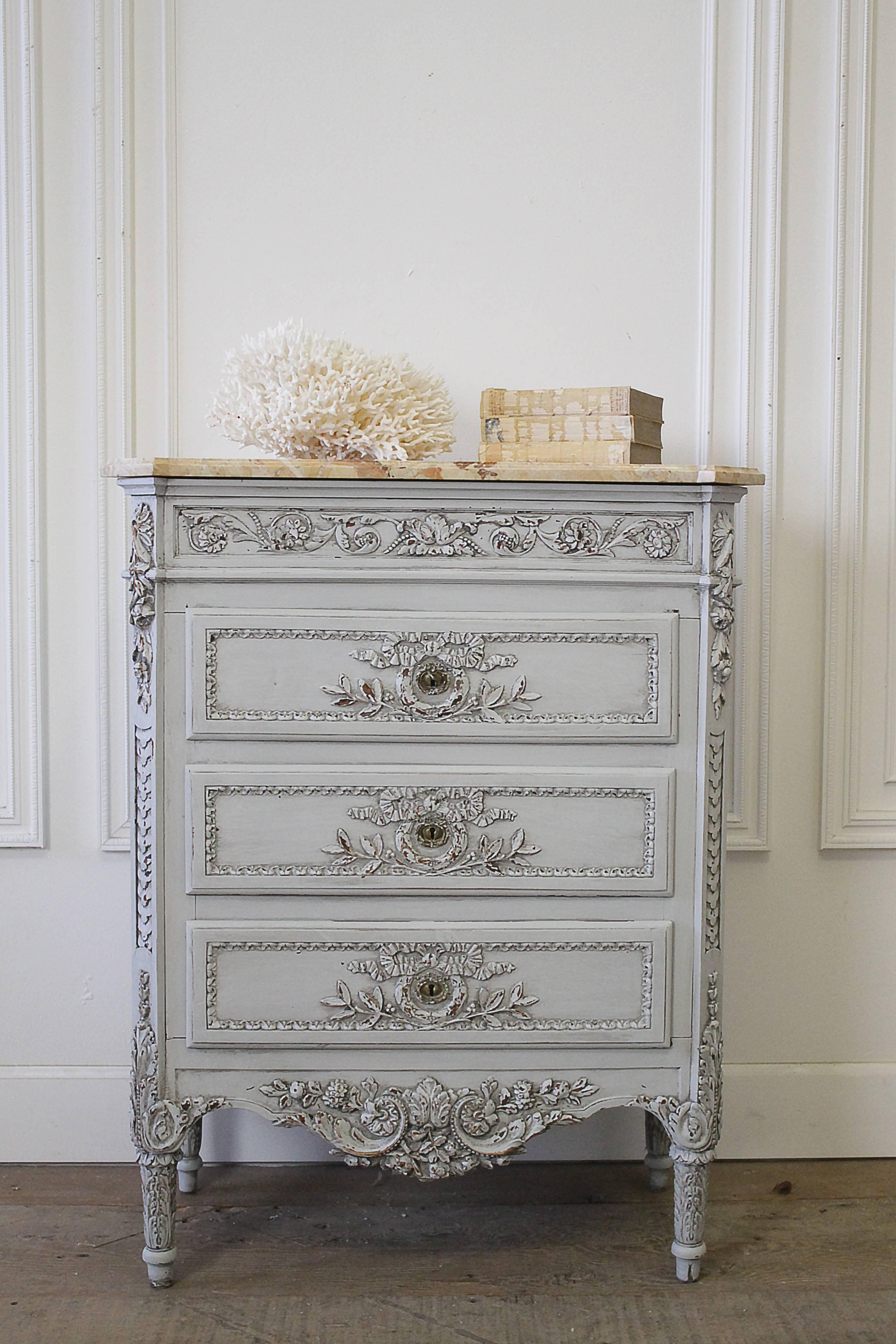 Lovely painted chest of drawers made in Belgium, with a dark cream golden tone top marble. The chest has a newly painted finish in a French grey, with light distressed edges. Beautiful intricate ribbon carvings, scrolls and roses. There is an