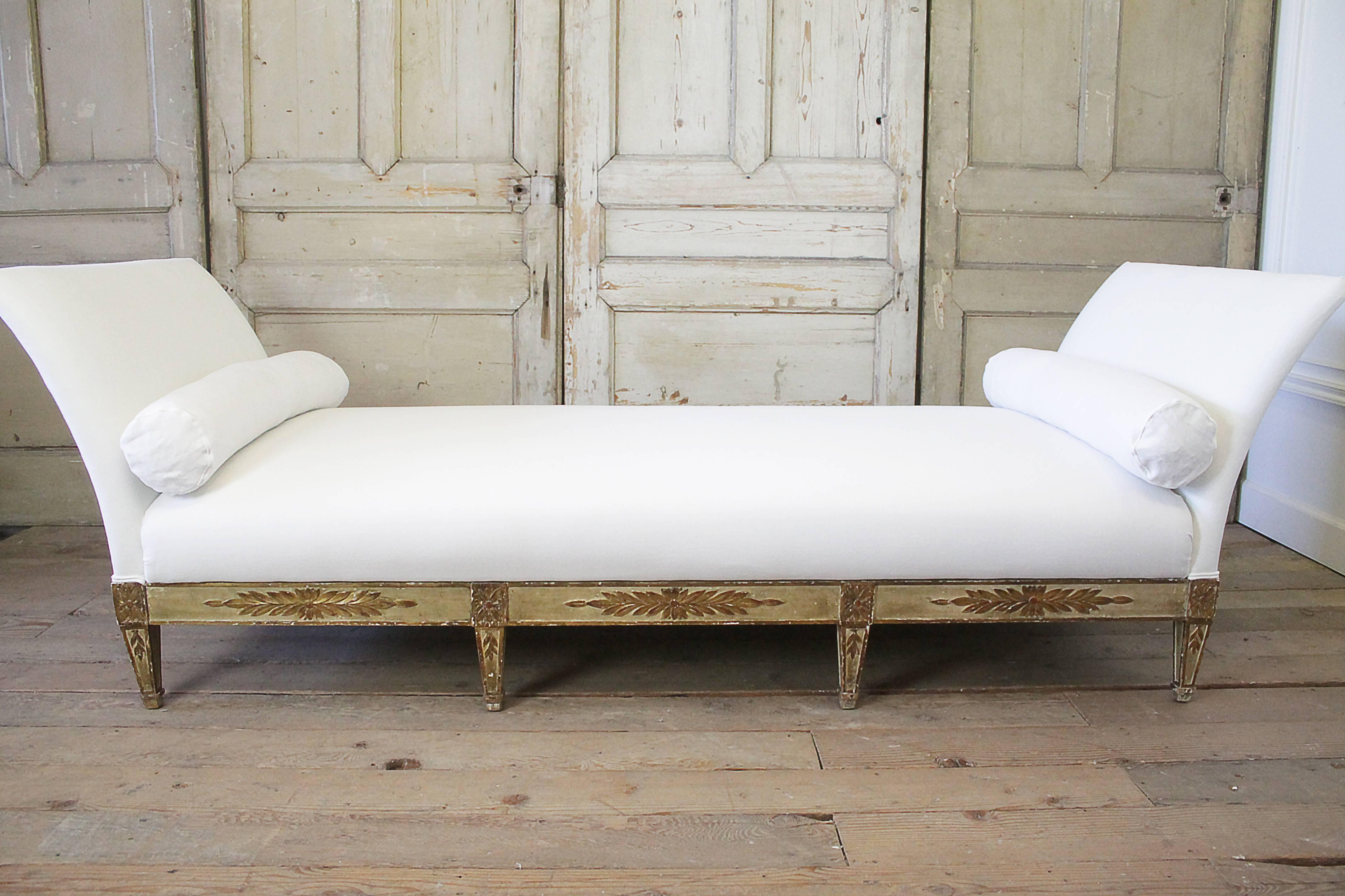 Beautiful painted and gilt daybed upholstered in 100% pure Belgian soft white linen. This daybed has original distressed chippy painted base and legs. It does come apart into five pieces. The headboard and footboard which are the exact same