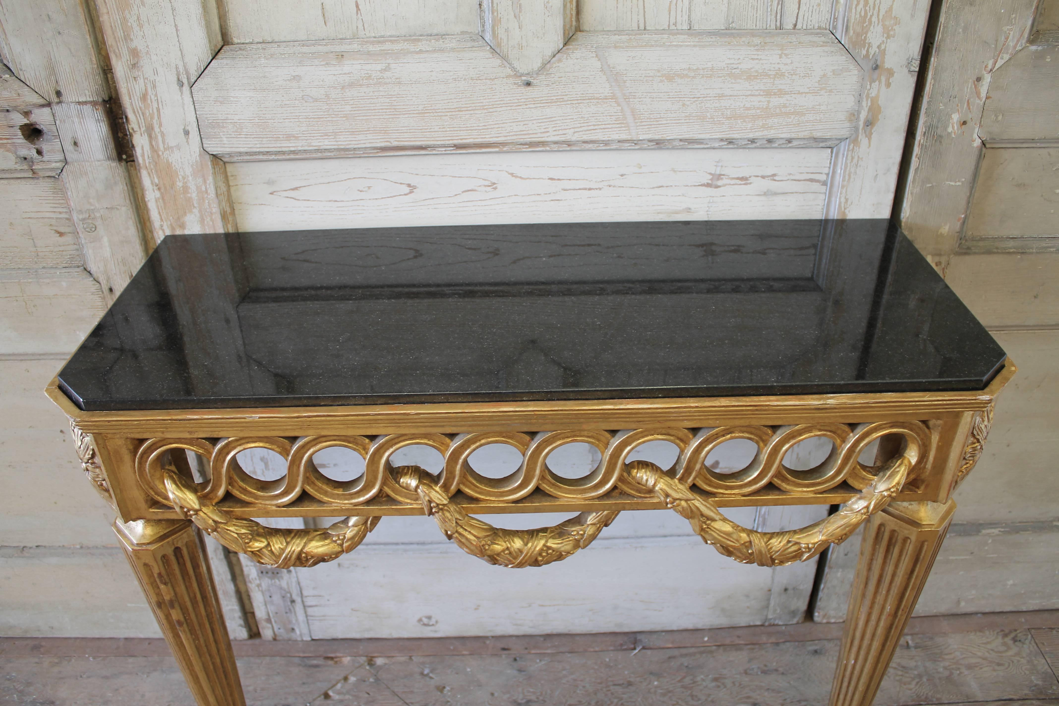 Beautiful neoclassical style wall console, with large laurel leaf swags roping through the front and sides.
Two Legs at the front corners, this console attaches to a wall easily with predrilled areas along the back.
The black marble inset is not