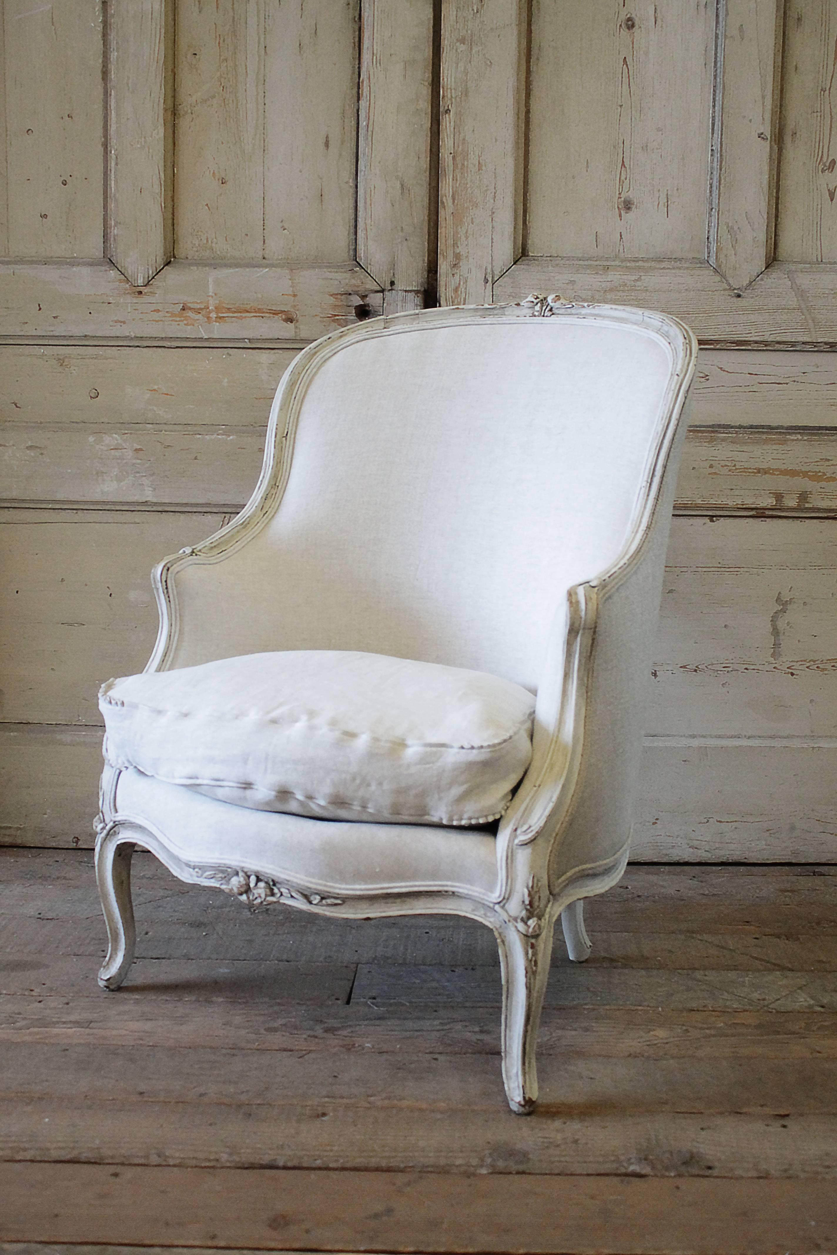 Lovely 19th century bergere chair painted in our oyster white finish with distressed edges, and antique glaze finish. The frame has a greyish tone patina. We reupholstered this chair in a soft heavy Belgian linen, the color is greige, which is a