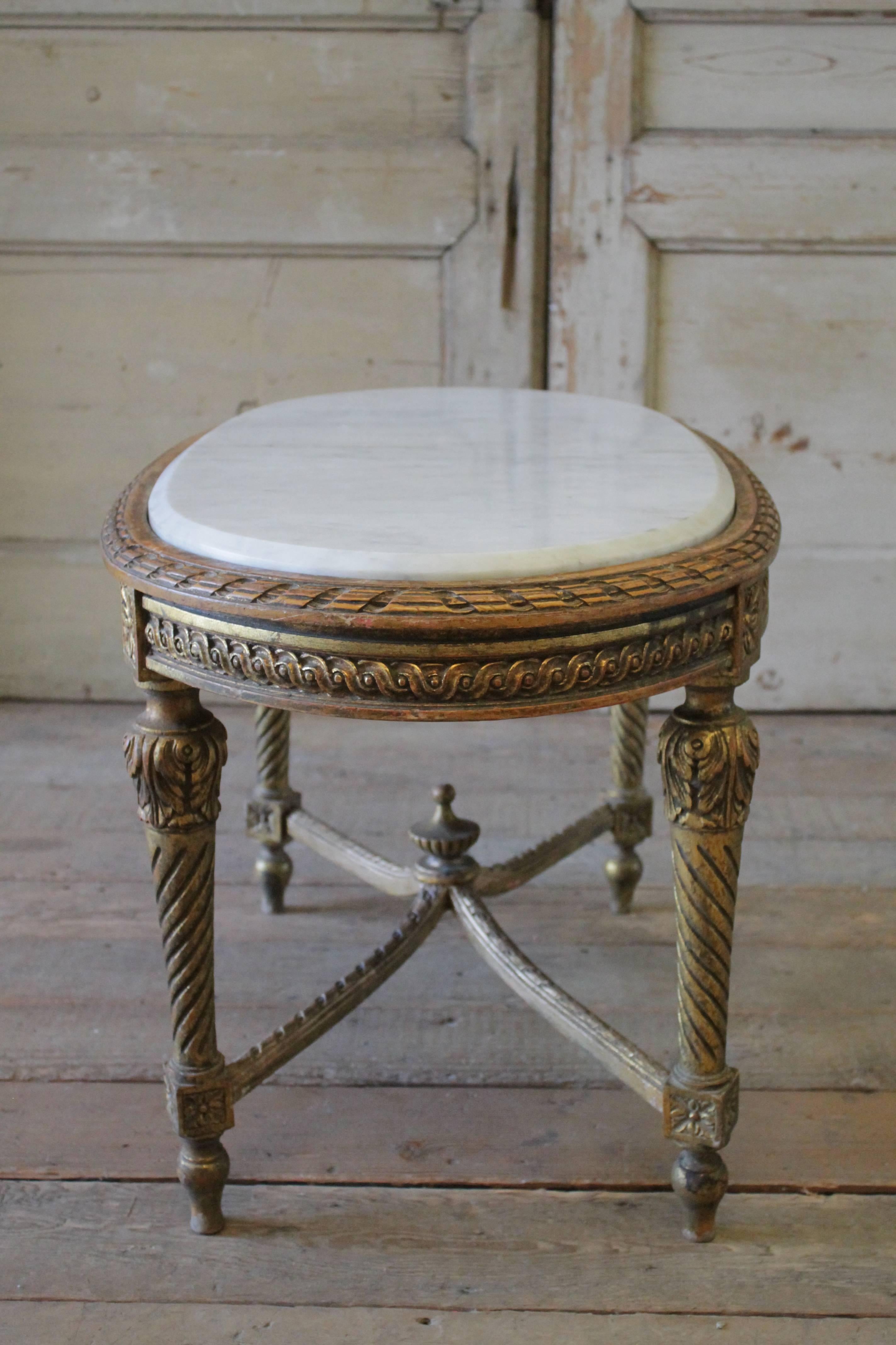 Beautiful antique French Louis XVI style coffee table has a weathered gilt finish. The white and grey vein marble top is in good condition with subtle signs of use.
The legs are sturdy, with a beautiful carved stretcher and carved finial base. A