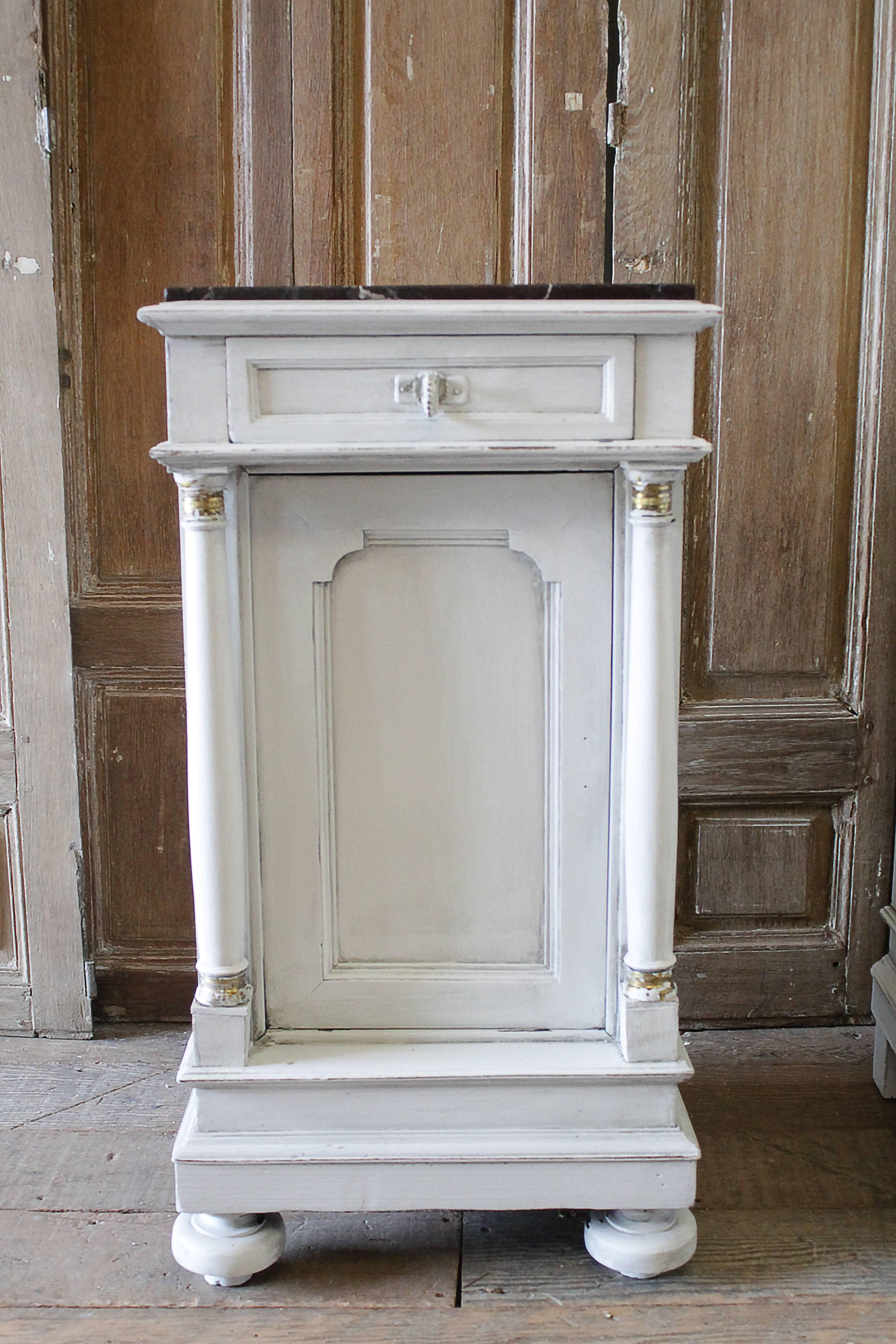 Petite bedside tables have been painted in a soft pale oyster grey, with subtle areas of distress, exposing beautiful brass details around the top and bottoms of the columns. The drawers have a brass pull, the bottom doors do open up, however they