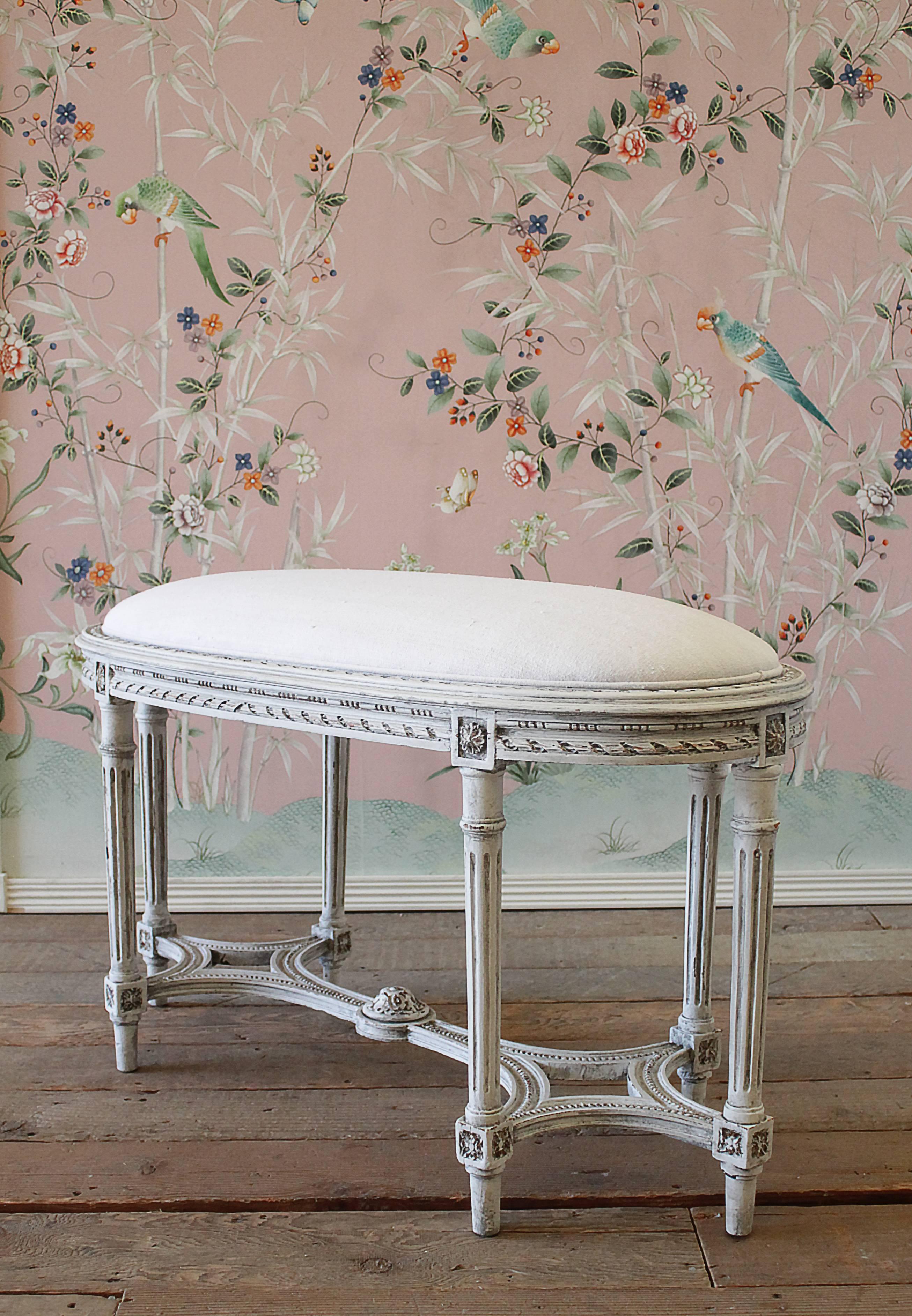 Antique Louis XVI style upholstered oval bench with six legs. Finished in our antique oyster white, with subtle areas of distressed edges, and finished with an antique glaze, to give the look of a time worn patina. We reupholstered this in 100 year