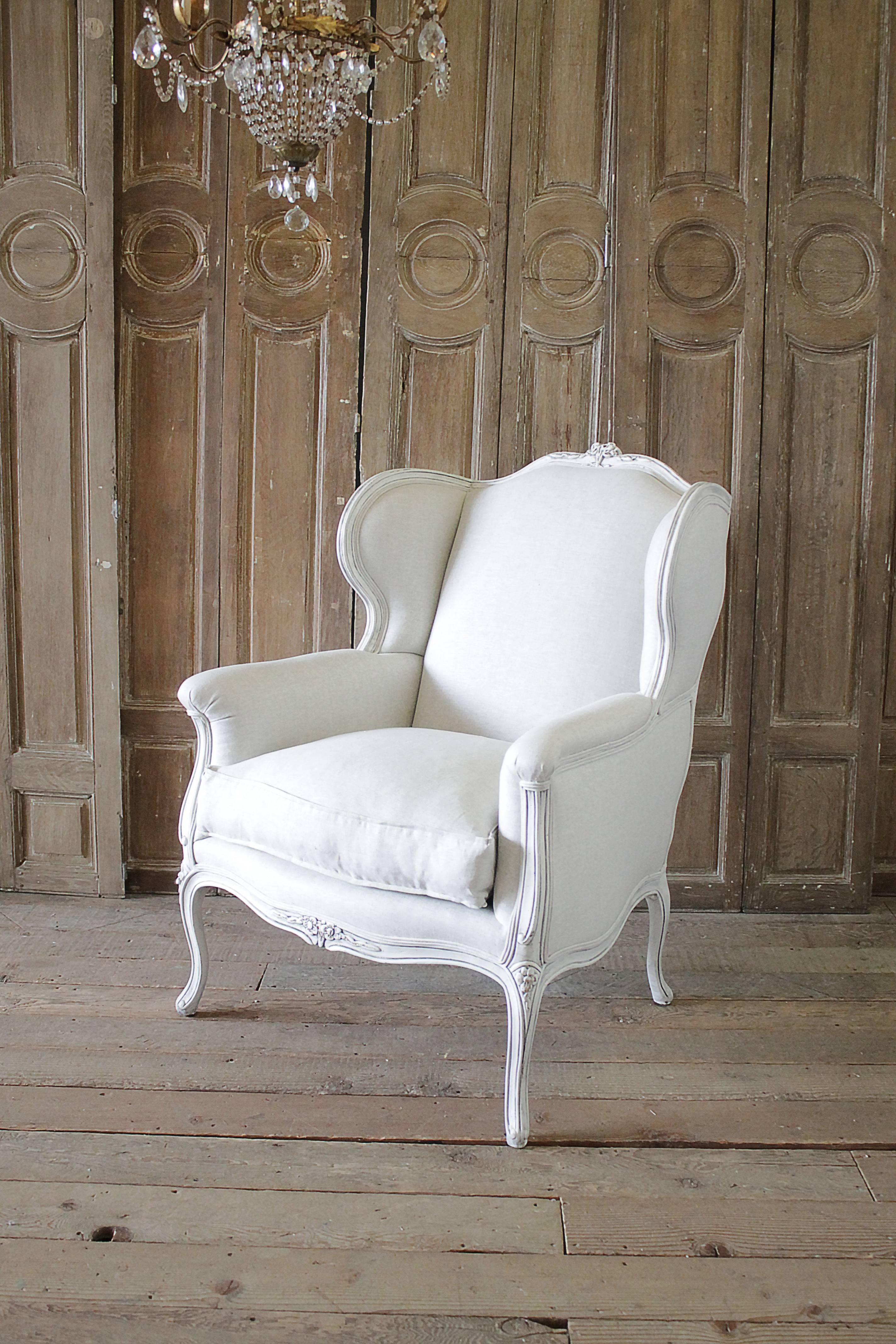 Early 20th century oversized Louis XV style wing chair, painted in our soft oyster white finish, with subtle distressed edges, and upholstered in a light natural linen, and double welt trim. The back of the chair has a slight pitch, so when you sit