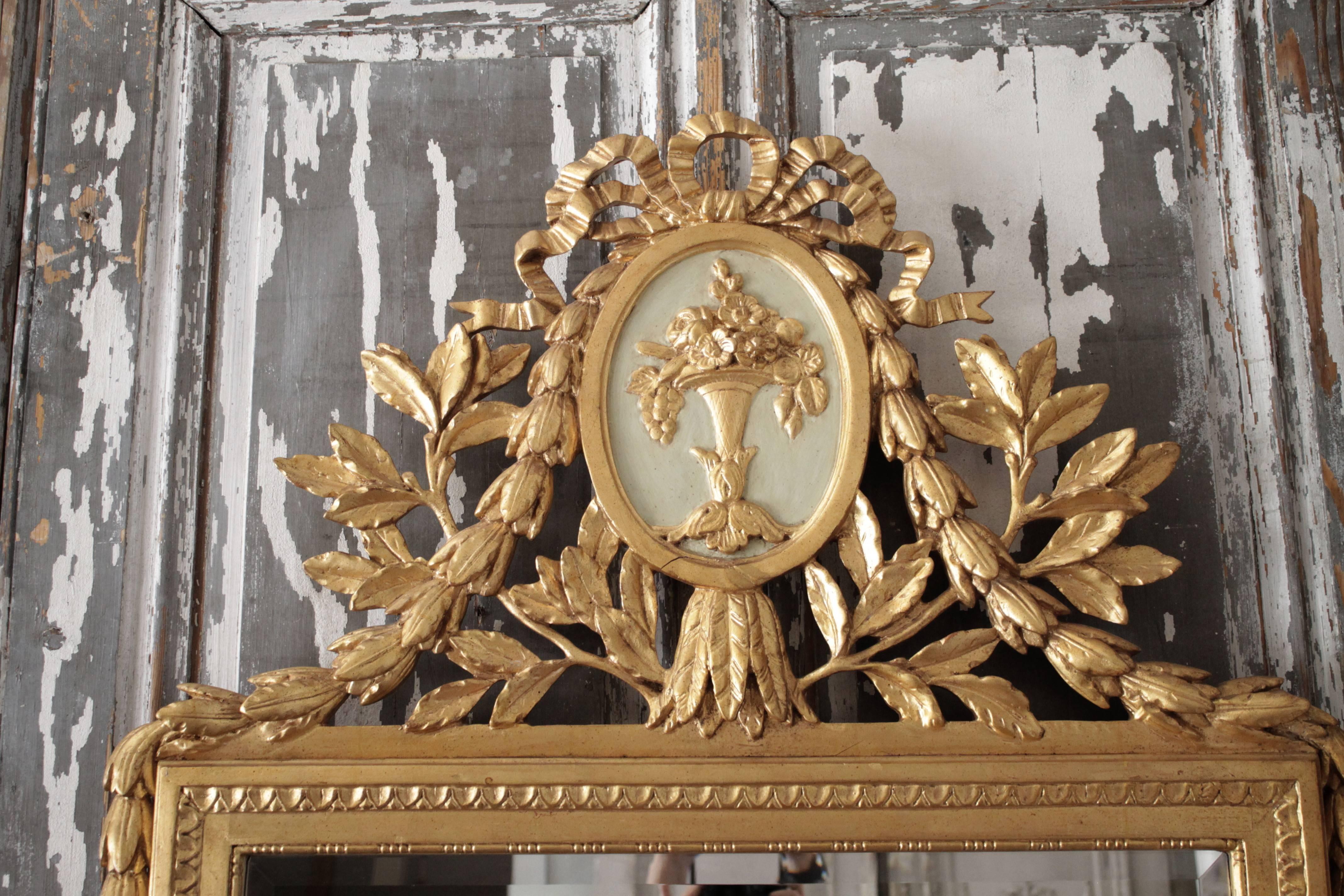 Elegant carved giltwood mirror with decorative elements typical of that period and style include an urn with fruits, flowers and leaves, as well as ribbons and pearls. Original beveled mirror has some aging.
