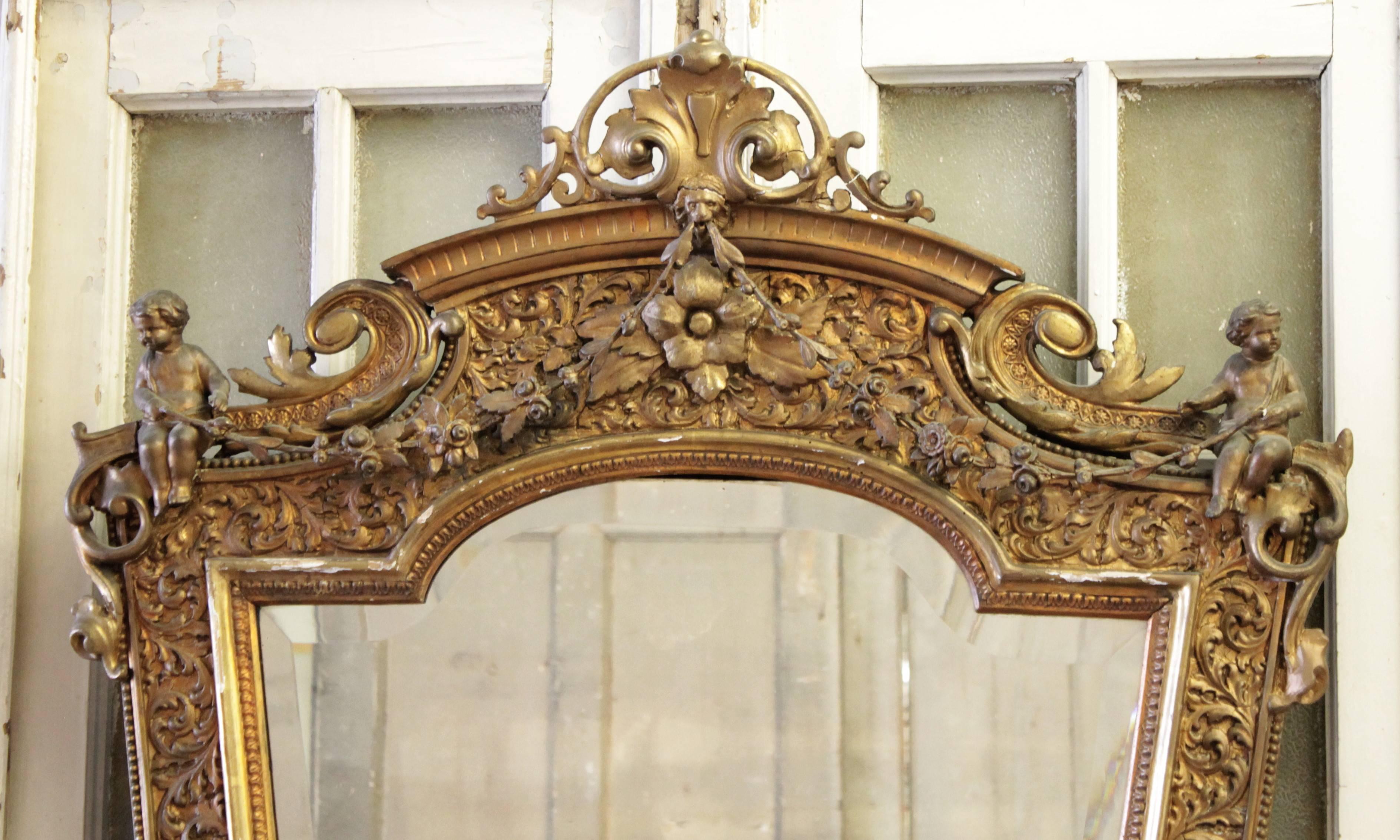 Pair of large French Louis XV figural hand-carved wood and gesso mirrors. The elaborate carved mirrors feature extended floral swags from the crest to each surmounted cherub. Original beveled mirrors have some aging.