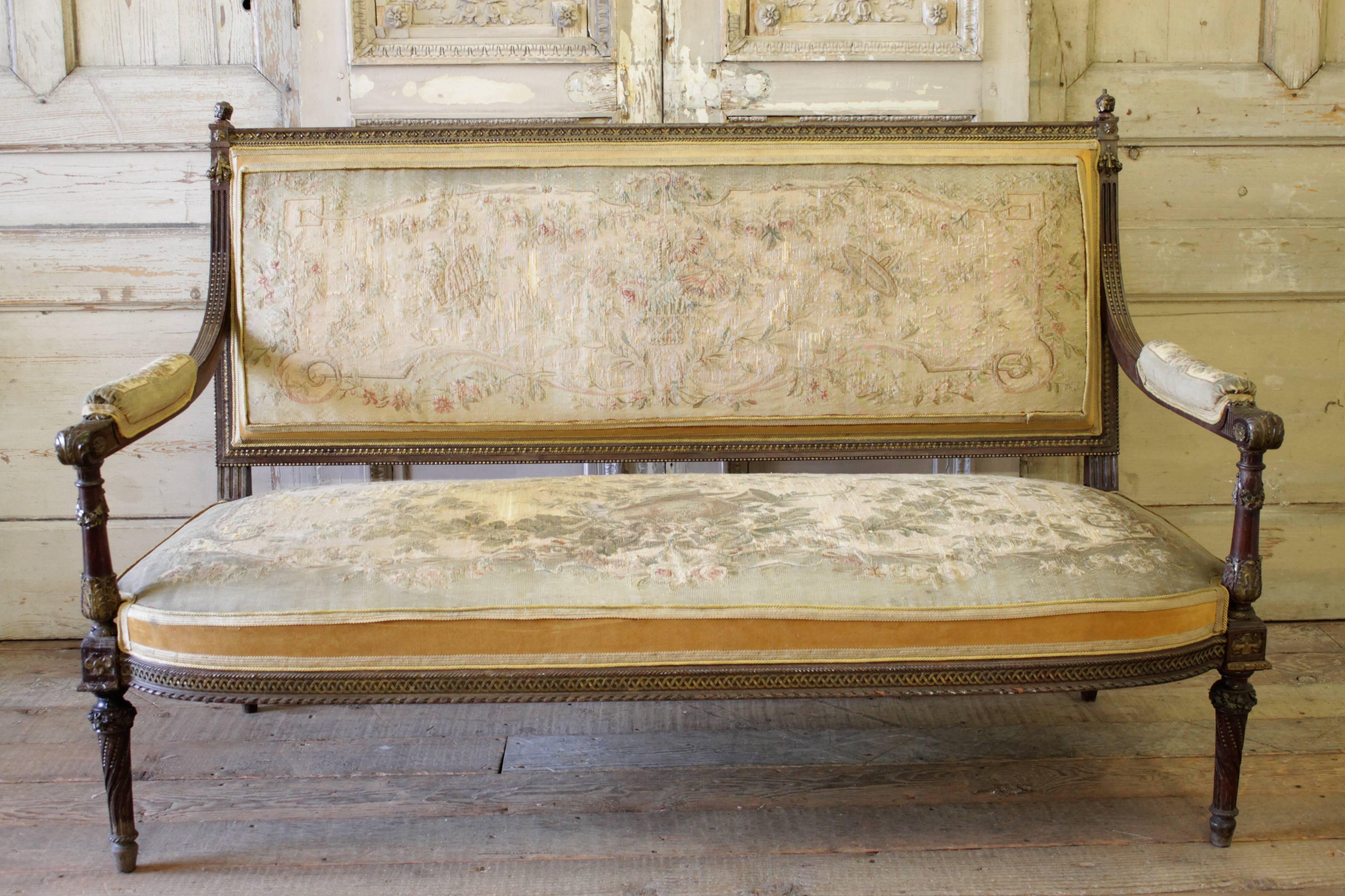 This beautiful Louis XVI style salon set has the original finish in wood and gilt carvings. Small carved rose swags adorn the backs and arms of each piece, with detailed carvings throughout the frame.
The original tapestry and velvet upholstery are