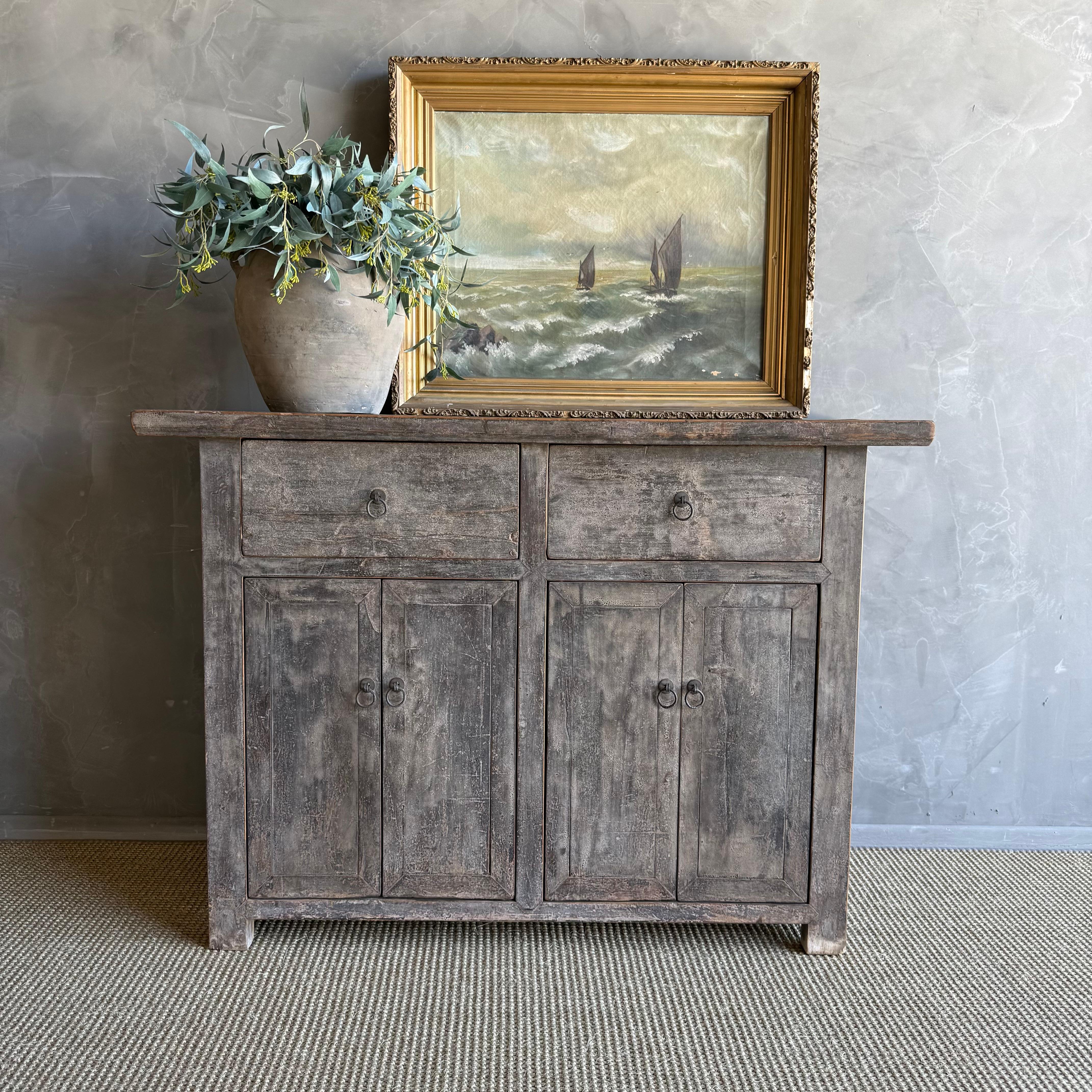 This charming vintage elm wood cabinet is a one-of-a-kind piece with beautiful age and patina that adds character to any space. Its patina painted elm wood finish showcases the natural beauty of the wood, while the solid elm wood original hardware