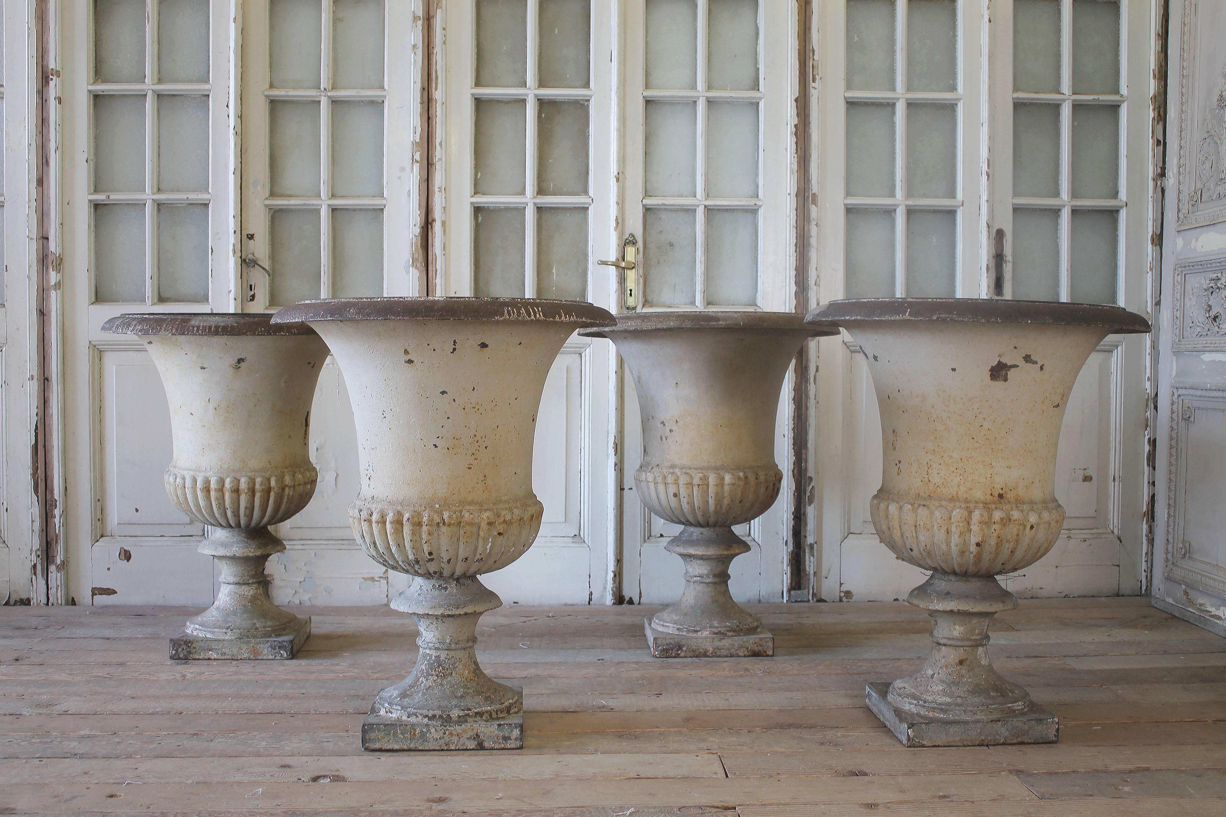 Four fabulous French urns with original painted finish. The coloring is a soft aged white that has weathered to a creamy, grey taupe finish. Wonderful crackle and aging to urns, and chippy paint here and there. All of the urns are solid and sturdy.