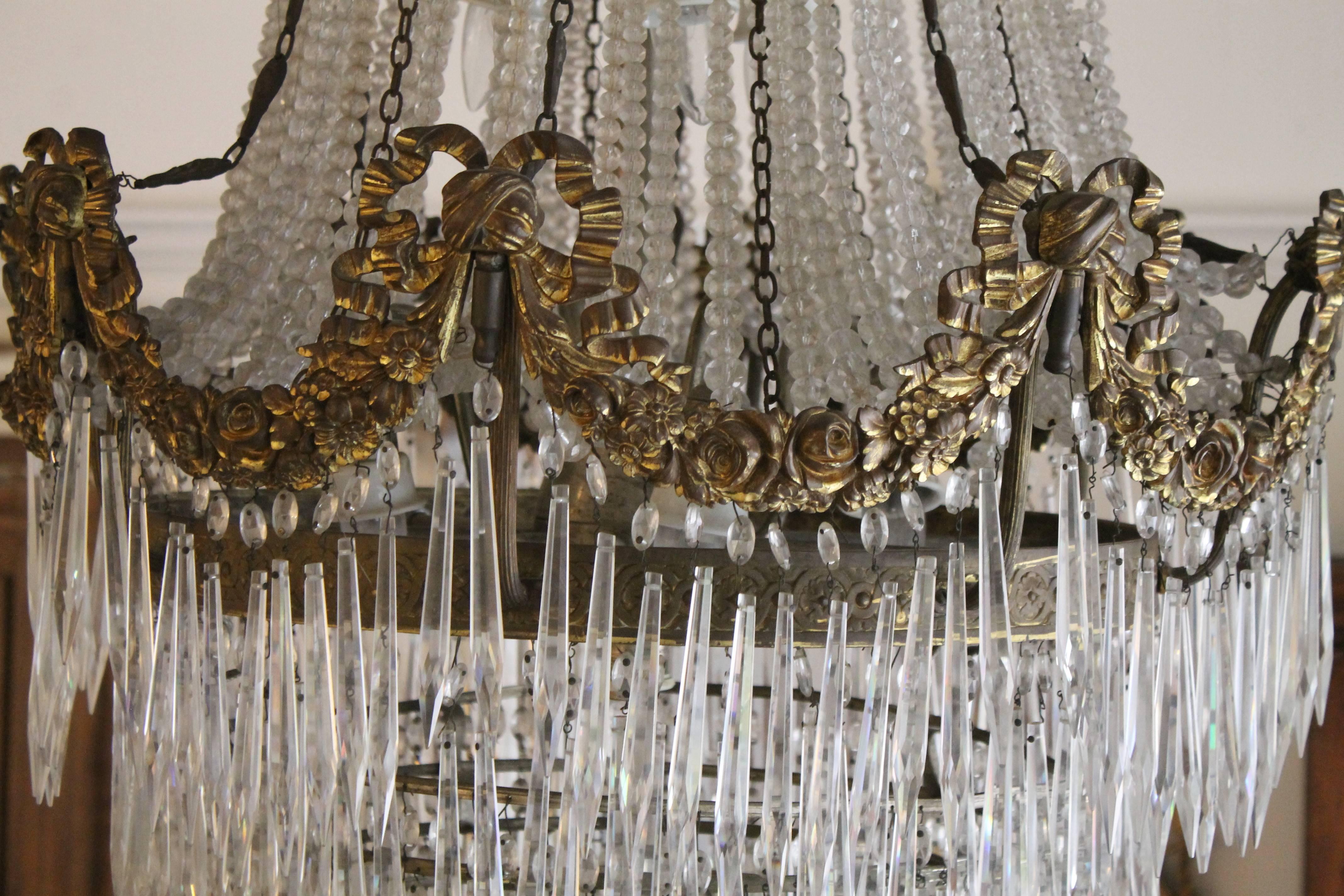 Large Empire eight-light ballroom style chandelier with nine layers of prism crystals at the bottom and finished with beautiful crystal prisms draped and accented with gilt bronze ribbons and rose swags. Finished in antique gilt over bronze
