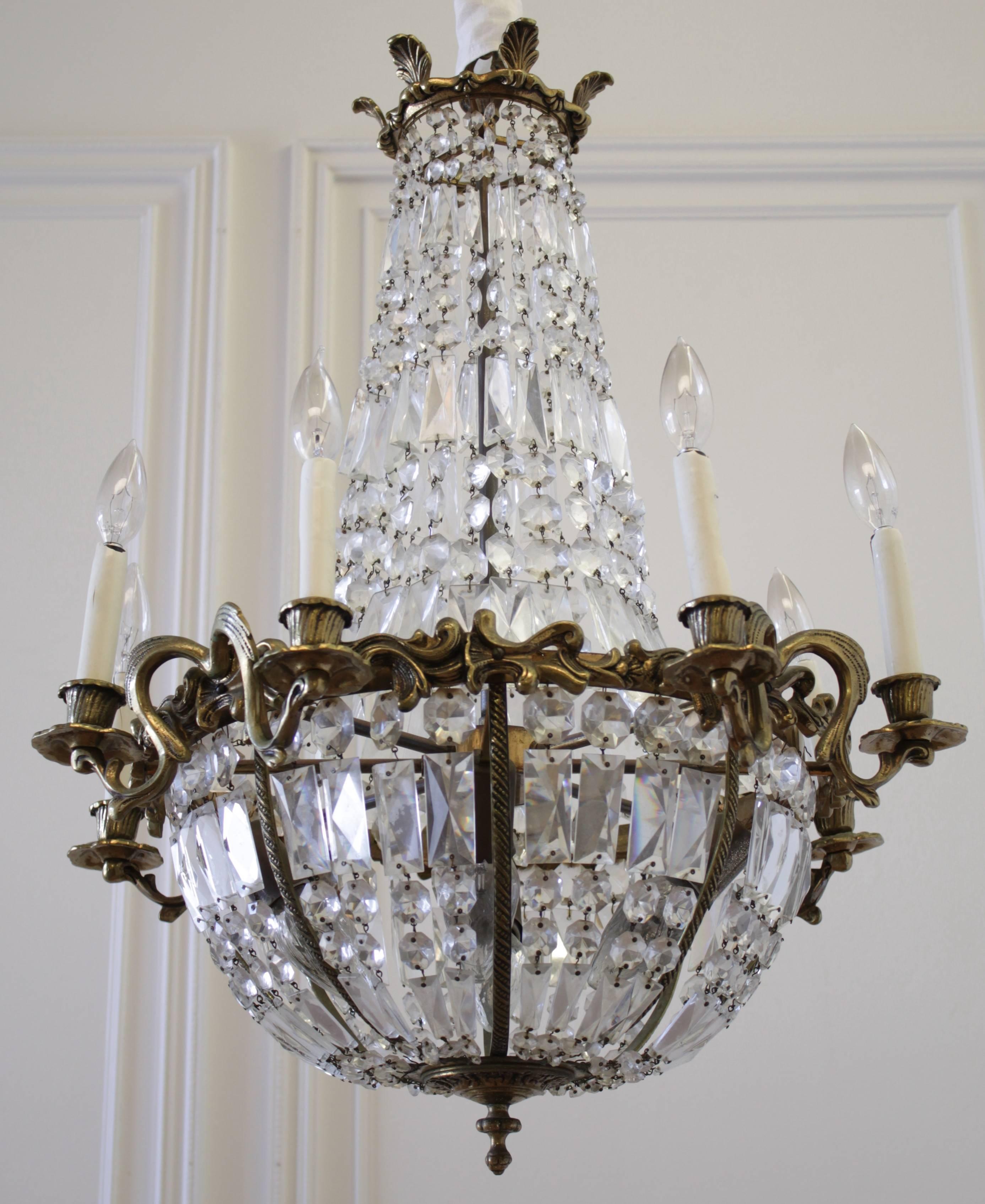Corbeille (Basket) chandelier in gilt bronze and crystal with eight outside light arms and four inside. Under the palmates gilt bronze crown flows out a string cascade of diamond shaped cutted crystals joining a large chased brass belt supporting
